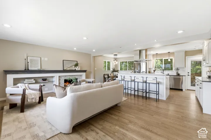 Open-concept living area featuring wood flooring, a contemporary fireplace with stone surround, a kitchen island with seating, white cabinetry, and stainless steel appliances