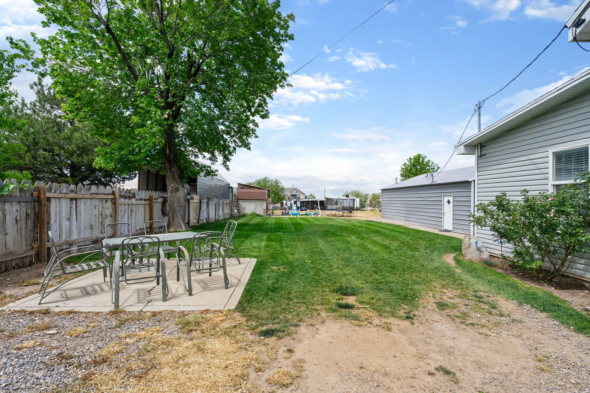 Expansive backyard featuring a large concrete patio, mature shade tree, and a wooden privacy fence