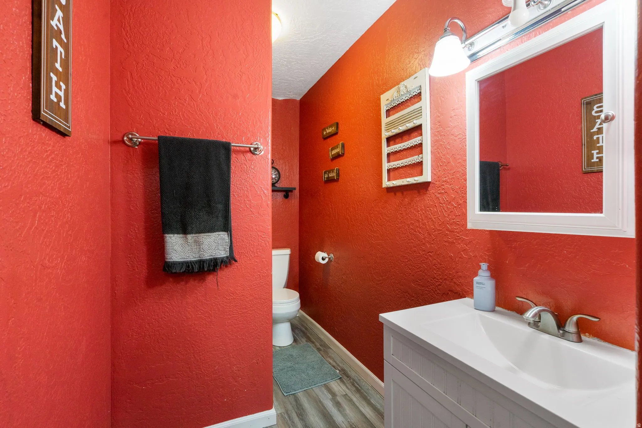 Powder room featuring a white single-sink vanity, integrated white countertop, and framed mirror with overhead lighting