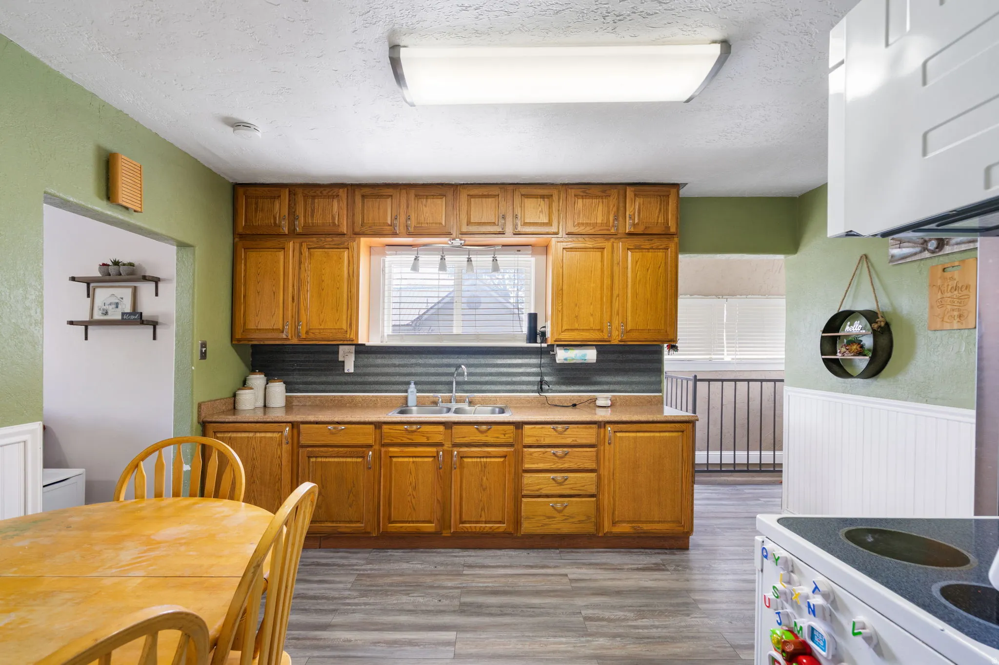 Kitchen featuring wood-finish cabinetry, a corrugated metal backsplash, and a double-basin sink with a window overhead