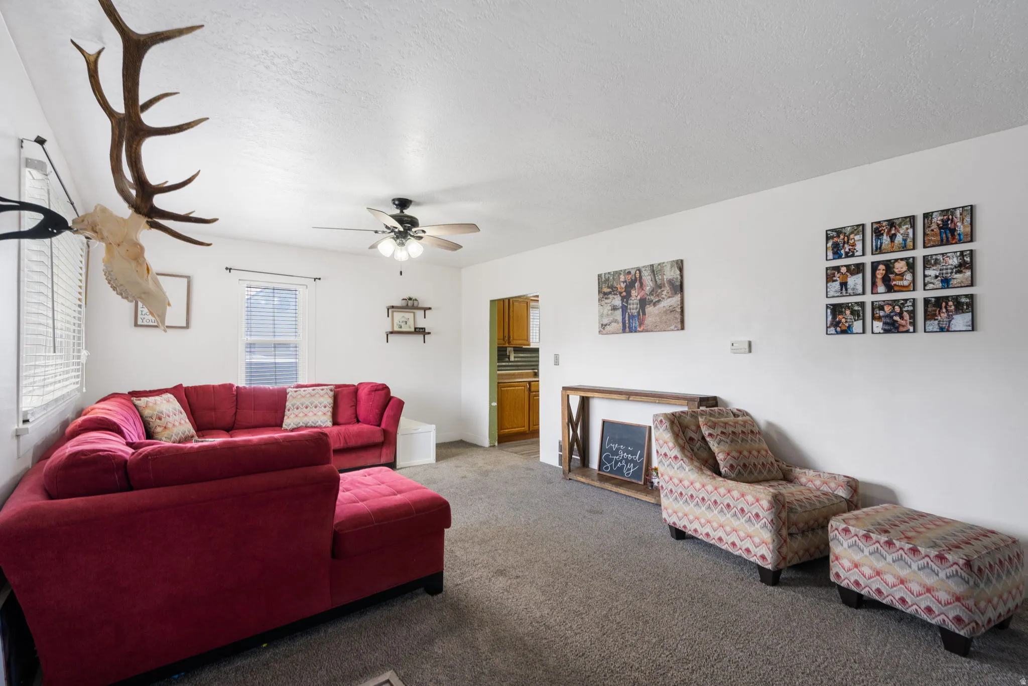 Living area featuring a ceiling fan, white walls, and carpet flooring
