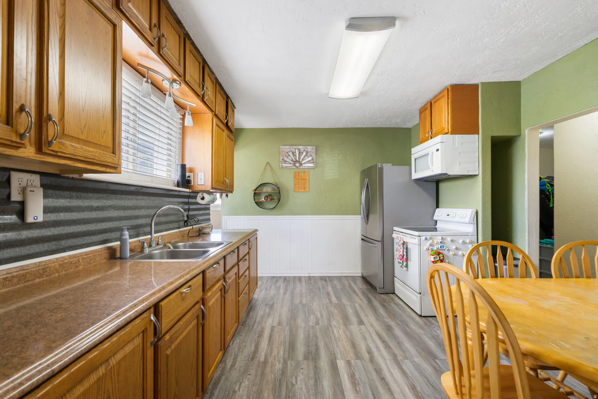 Kitchen featuring wood-finish cabinetry, laminate countertops, a double basin stainless steel sink, and a corrugated metal backsplash