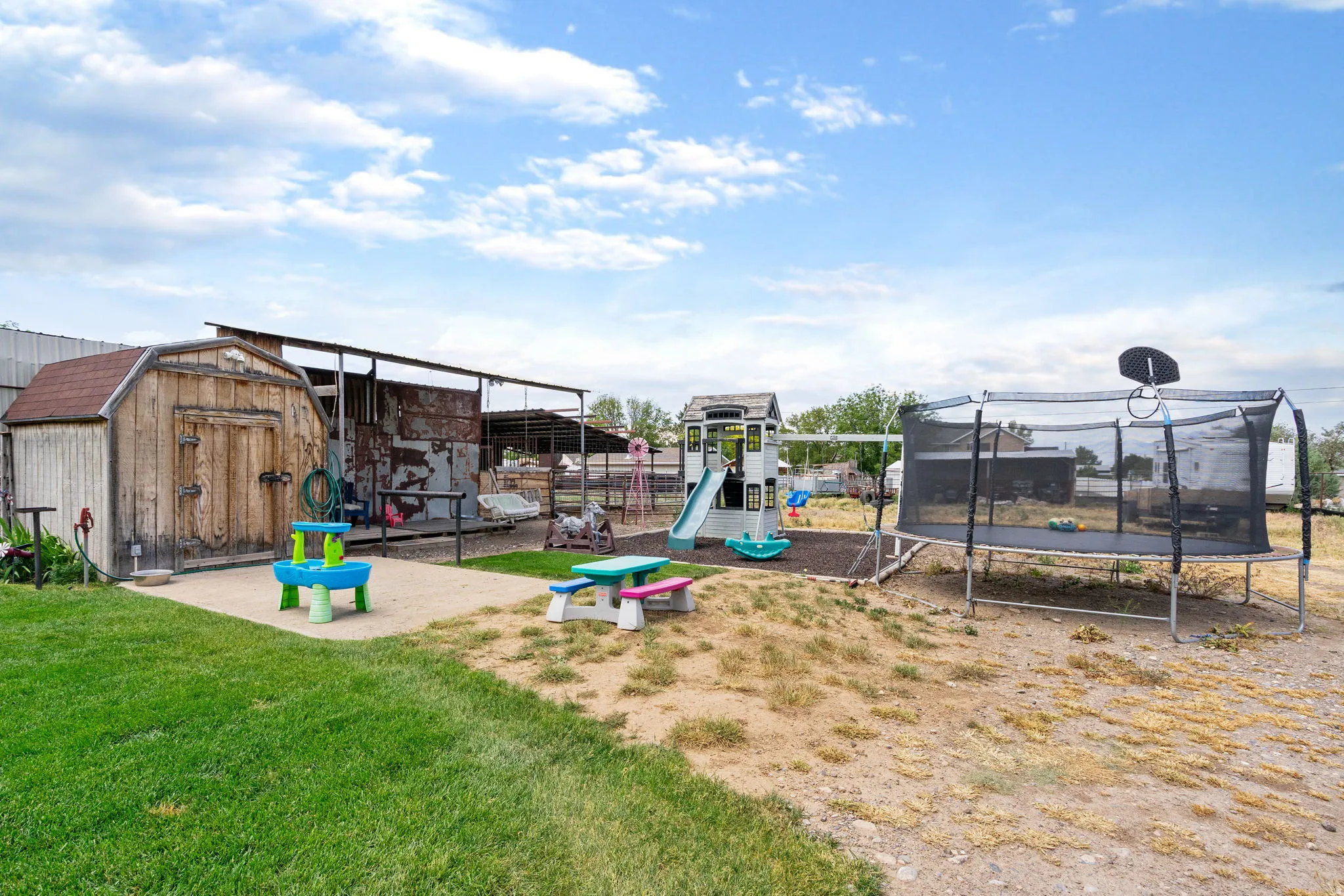 Expansive outdoor space featuring a detached storage shed with a gambrel roof, an open-air covered structure, a combination of manicured lawn and natural ground, and a clear sky overhead
