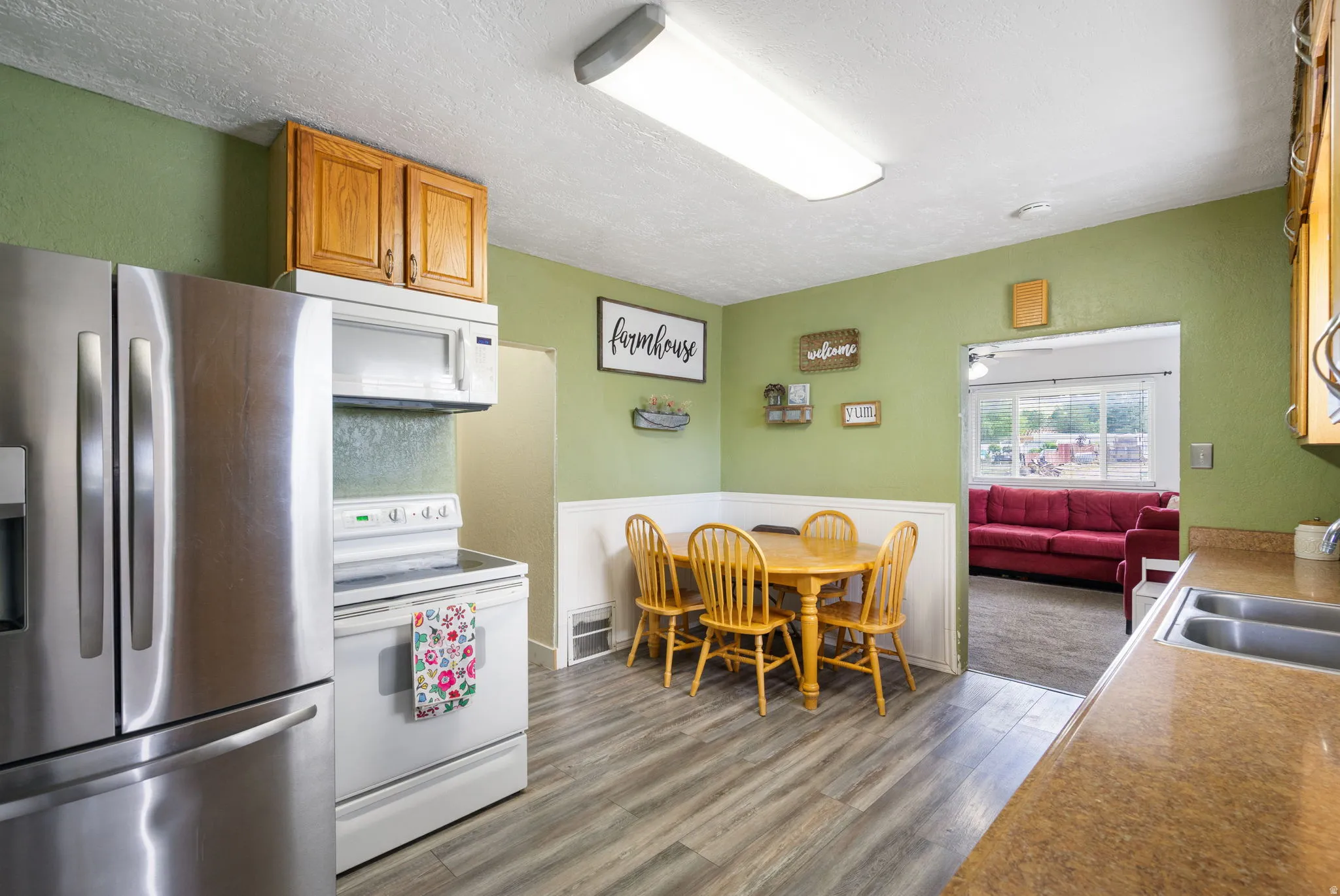 Kitchen featuring wood-finish flooring, stainless steel refrigerator, white range, wood cabinetry, and a double basin sink