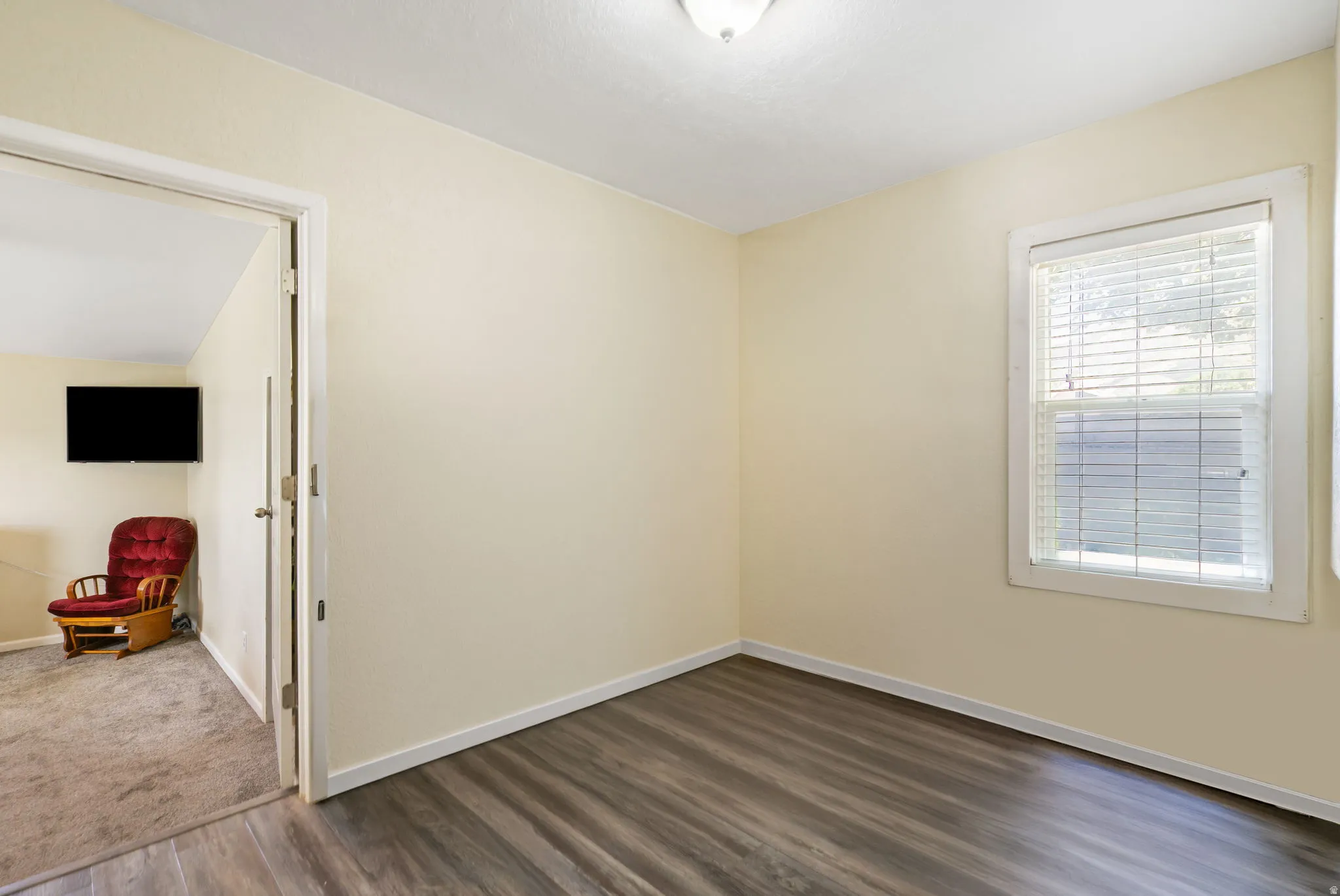 Room featuring wood-finish flooring, light cream walls, white baseboards, and a window with white blinds