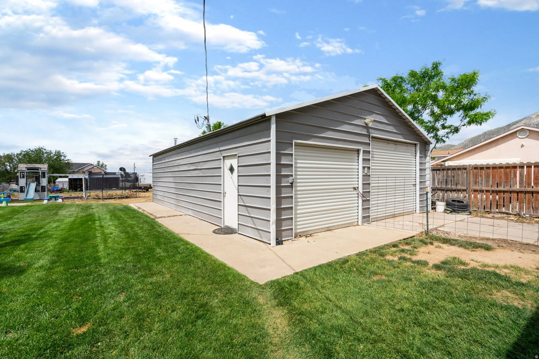 Detached metal garage with two roll-up doors, a single entry door, and concrete apron