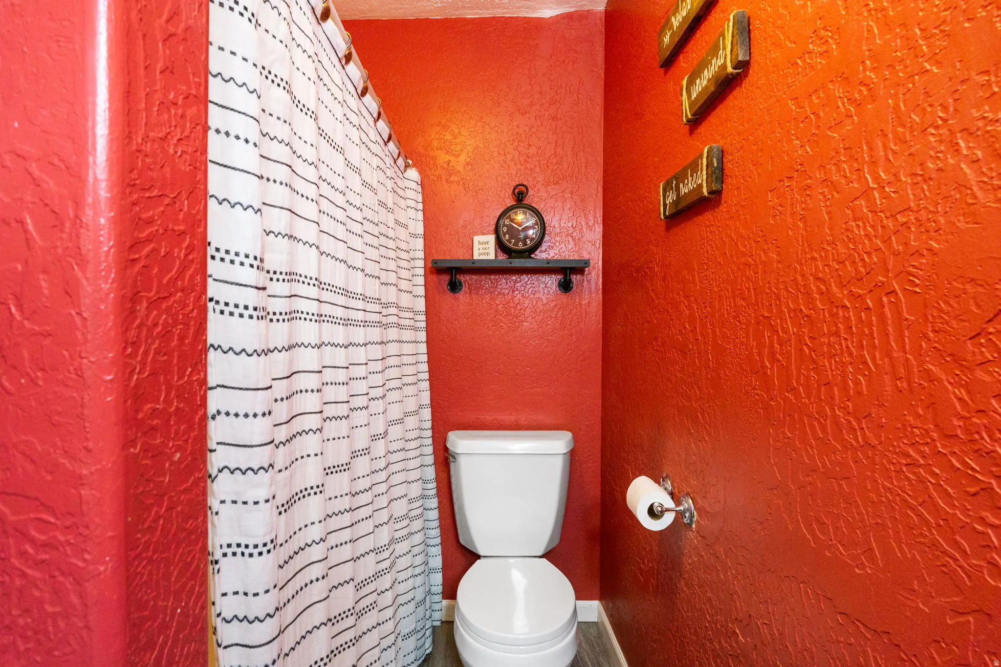 Contemporary bathroom featuring textured red walls, a white toilet, and wood-finish flooring