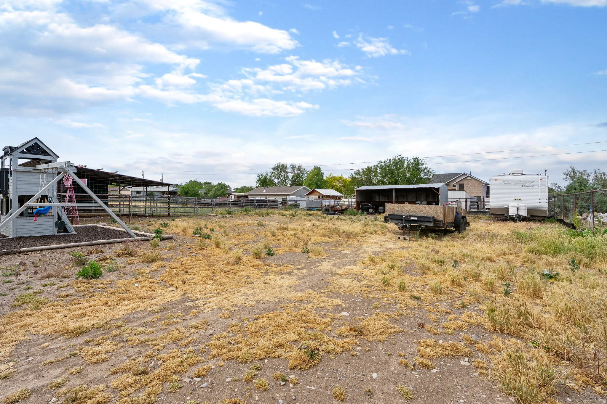 Expansive lot featuring a structured playset, covered outdoor storage, and perimeter fencing