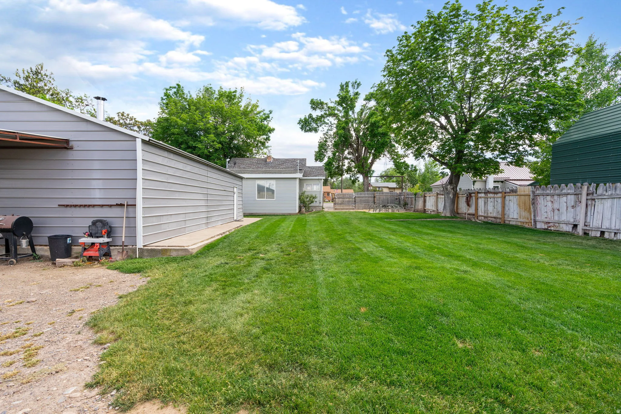Expansive grassy yard featuring mature trees and a perimeter fence