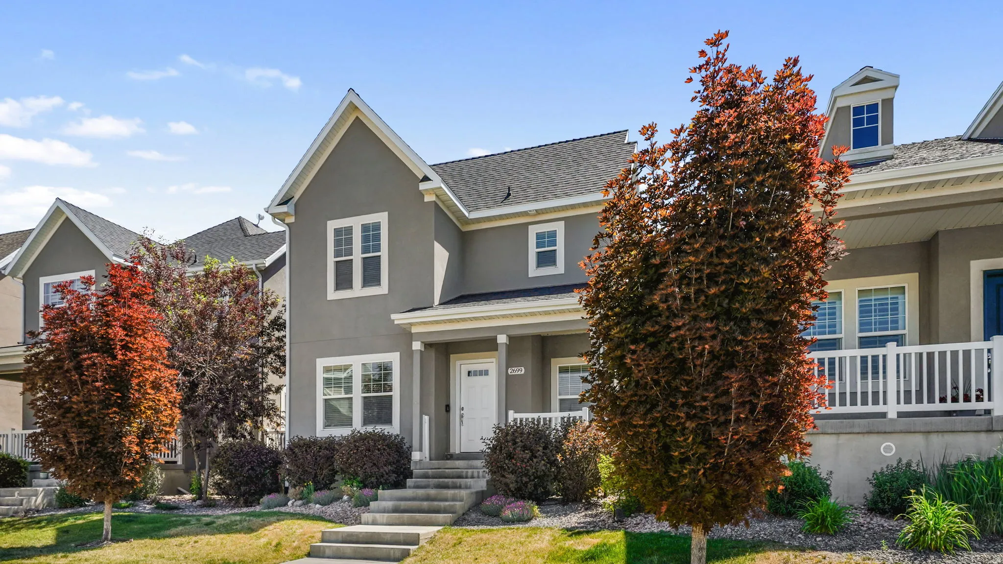 Gray stucco exterior with white trim, featuring a covered porch, a white front door, and a multi-level concrete walkway