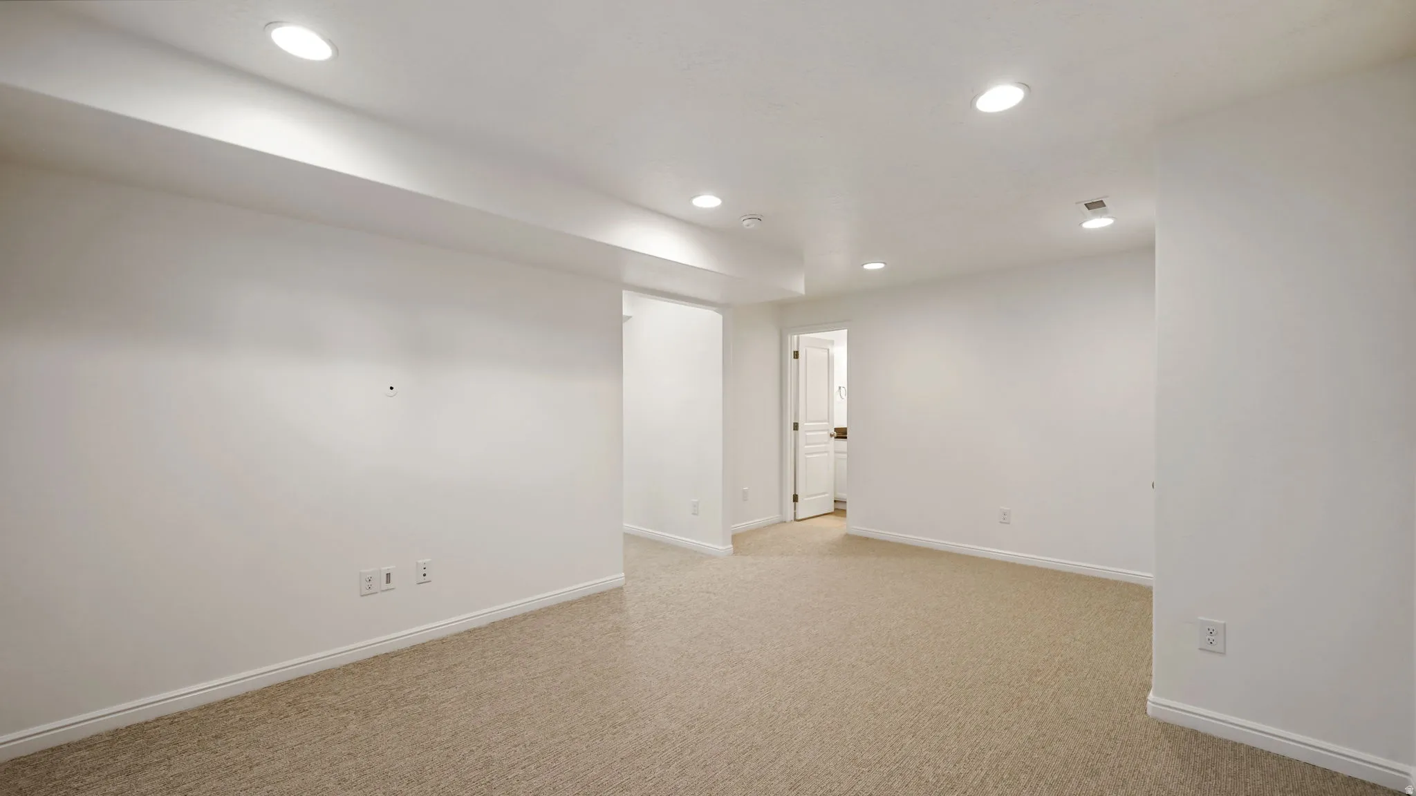 Spacious room with light-colored carpet flooring, white walls, and recessed ceiling lighting