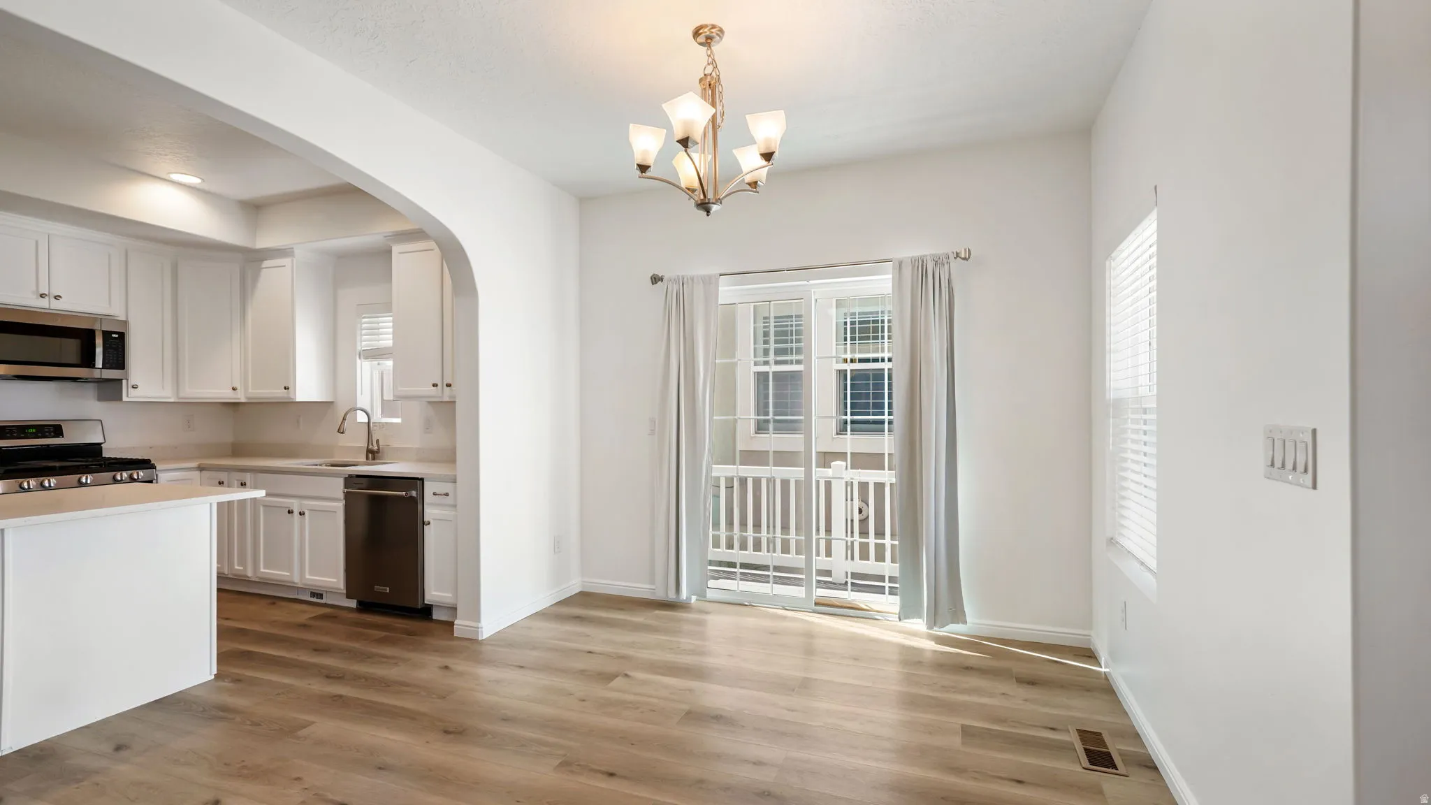 Spacious dining area with light wood-finish flooring and a contemporary chandelier