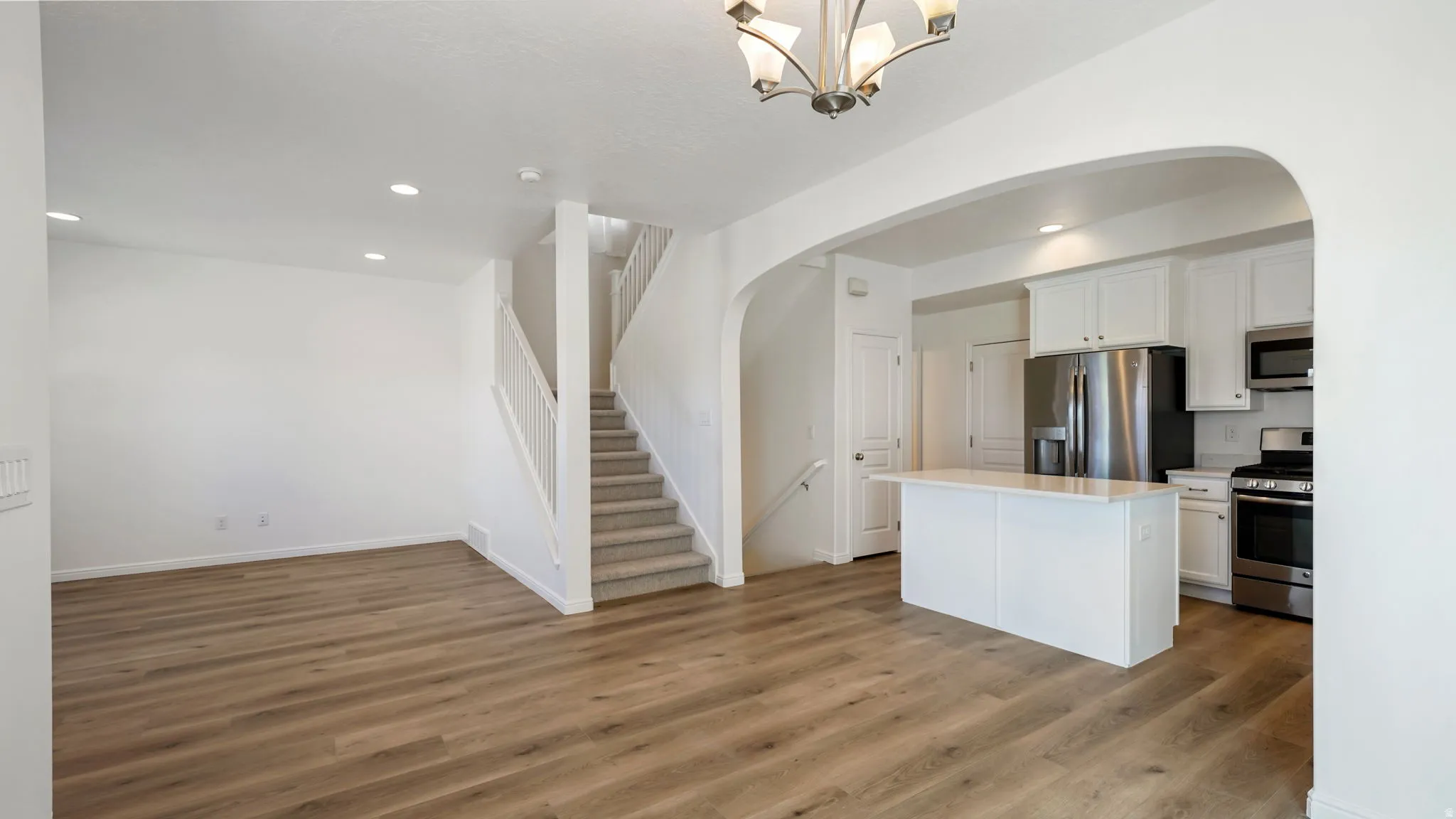 Open-concept living space featuring wood-finish flooring, recessed lighting, and a staircase with carpeted treads