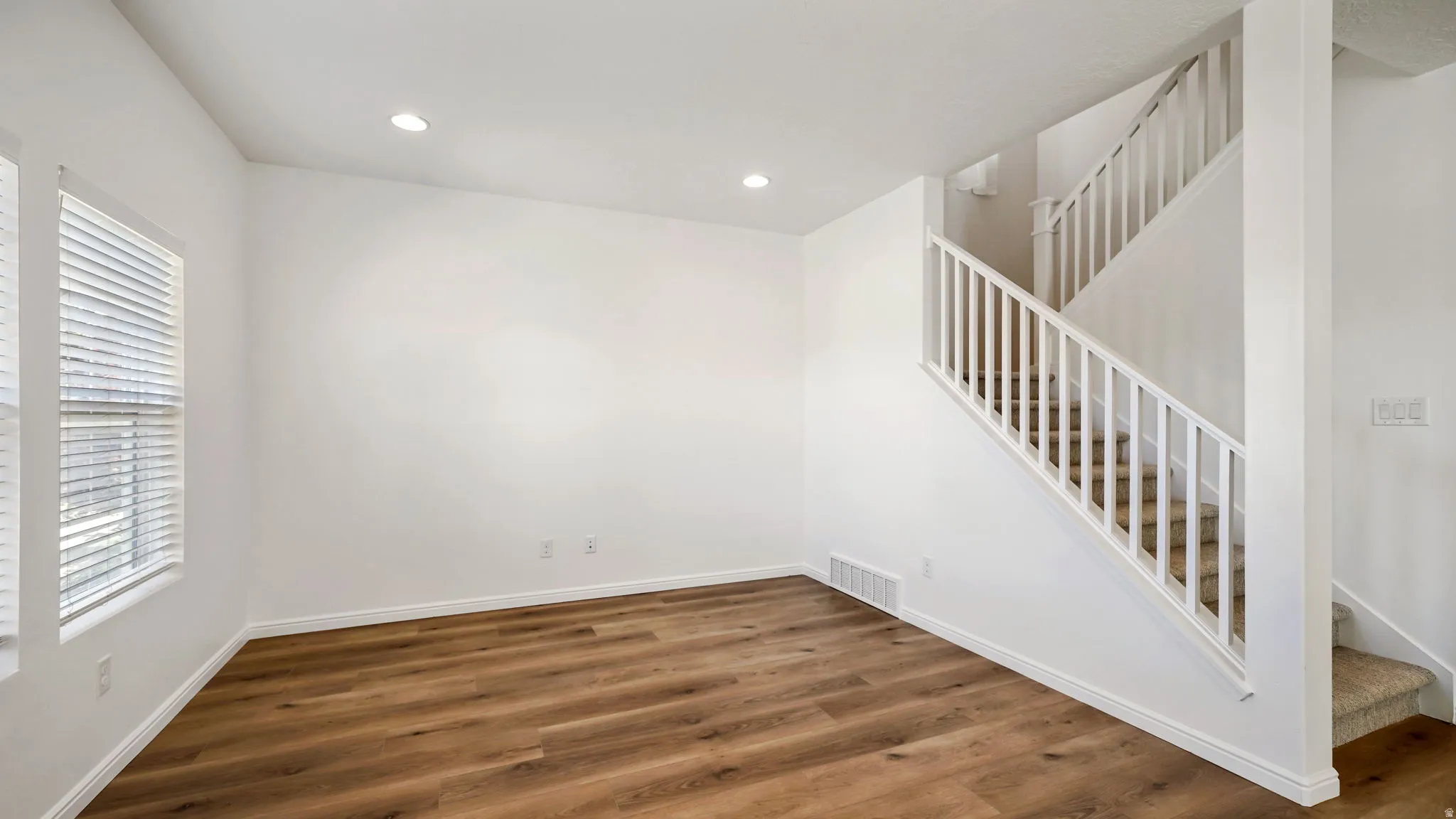 Spacious room featuring wood-finish flooring, white walls, and recessed lighting