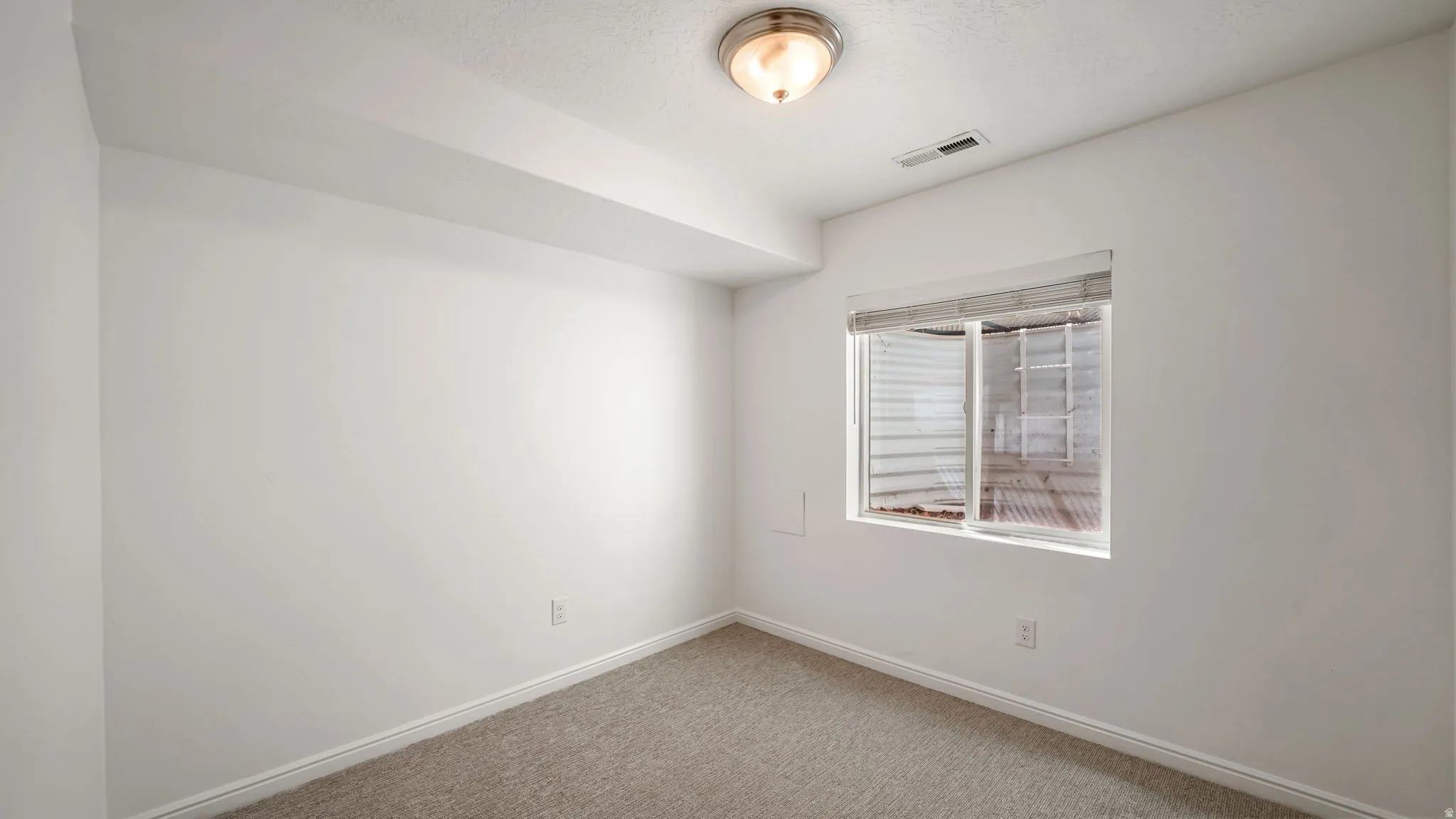 Room featuring a window with blinds, recessed ceiling beam, light neutral carpeting, and a flush mount ceiling light fixture