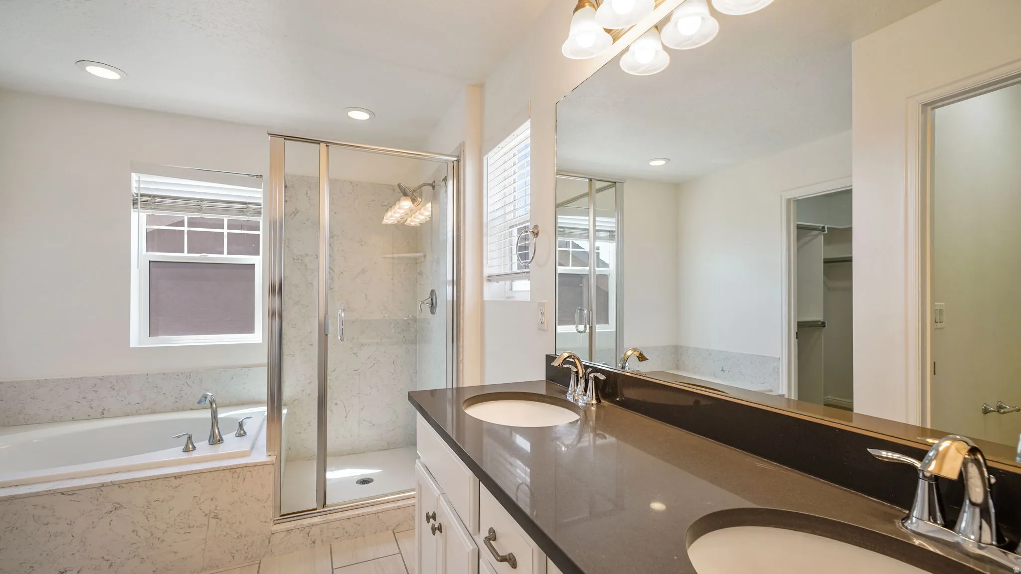 Dual vanity with an expansive countertop, integrated sinks, a full-width mirror, a separate shower enclosure, and a built-in tub with a coordinating tile surround