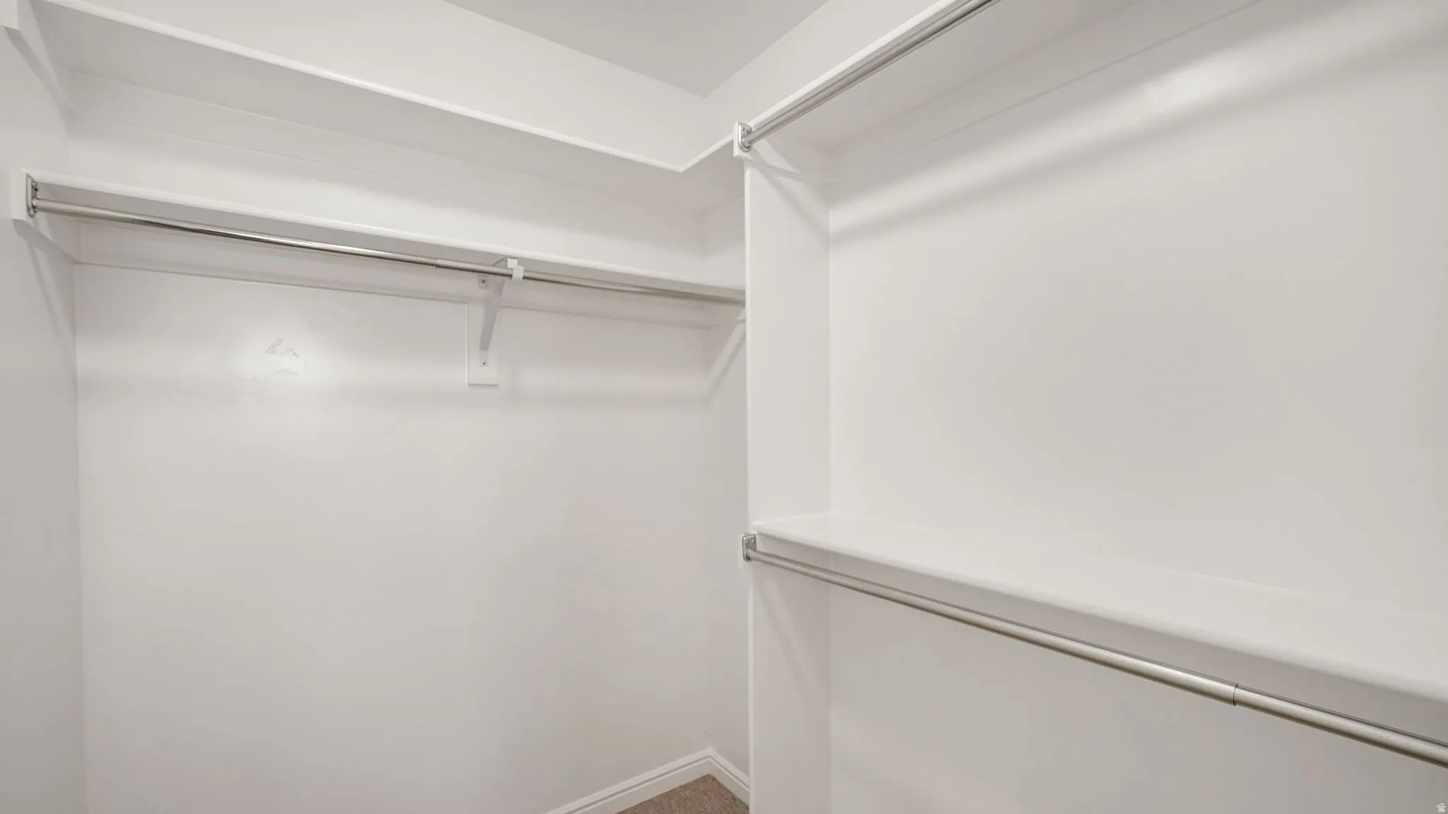 Walk-in closet featuring white shelving and chrome hanging rods