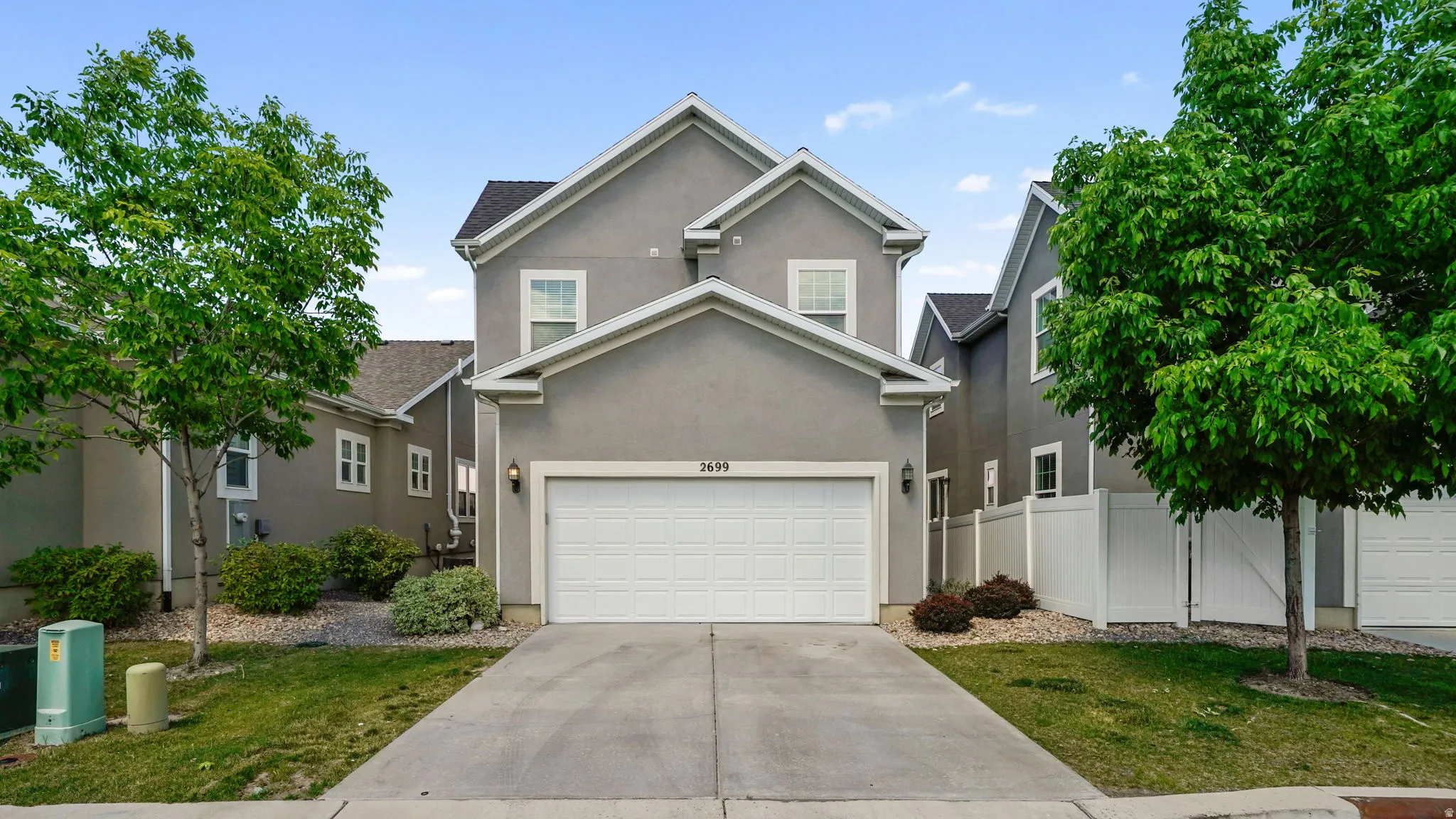 Stucco exterior with a two-car garage, concrete driveway, and mature landscaping