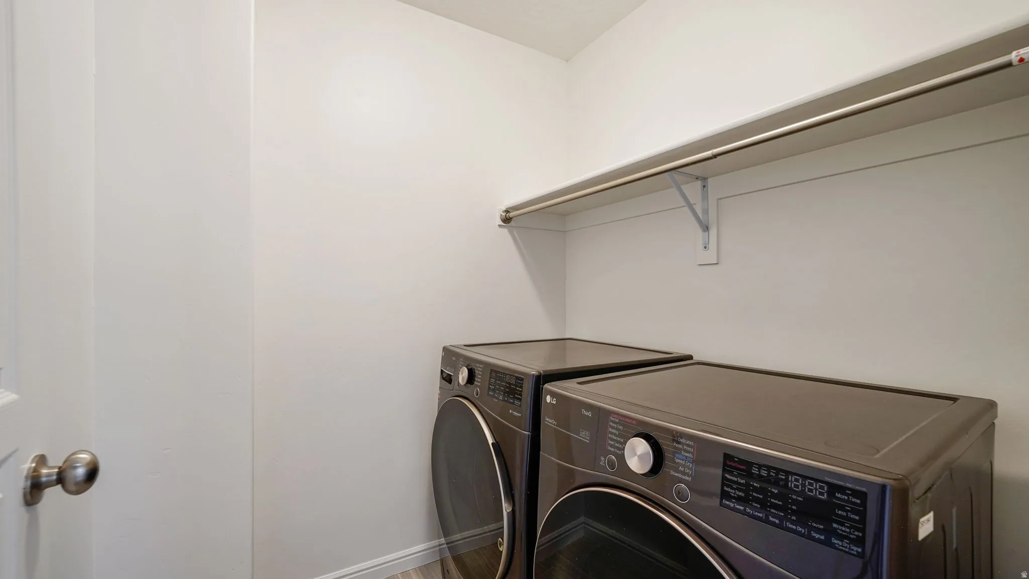 Dedicated laundry space featuring a white wall shelf with an integrated hanging rod and wood-finish flooring