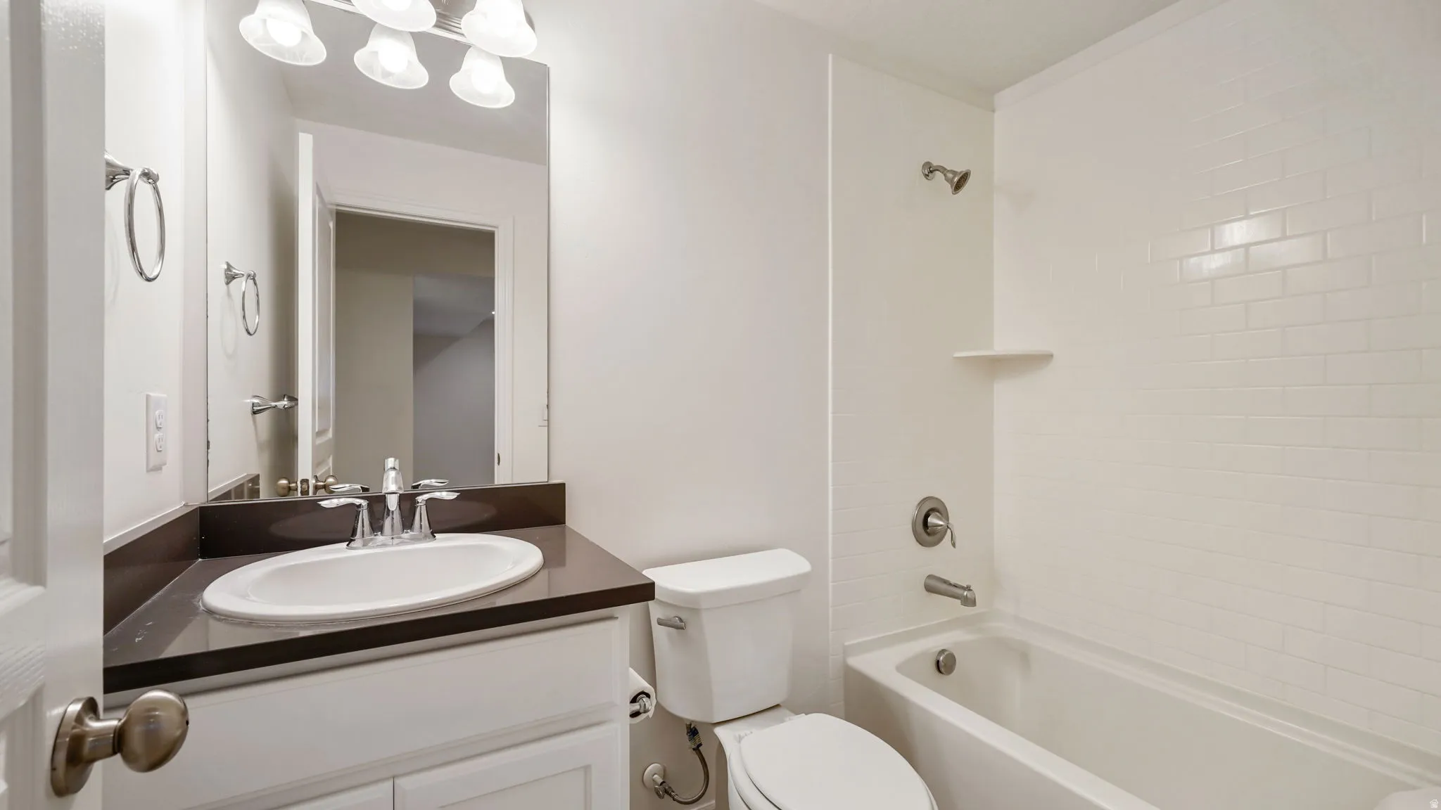 Bathroom featuring a white subway tile shower surround, a white bathtub, and a vanity with a dark countertop and a white undermount sink