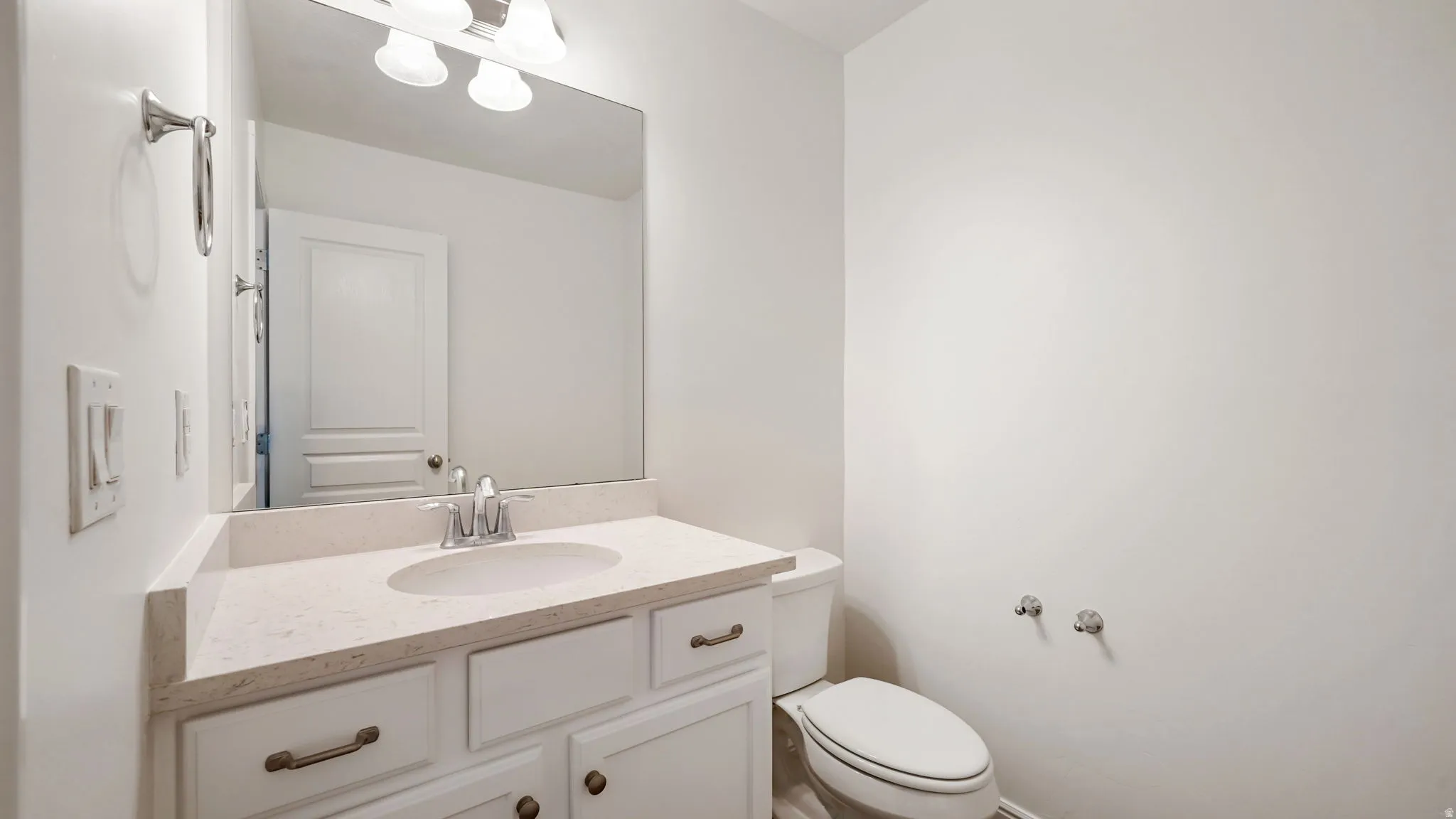 Bathroom vanity featuring a light-colored countertop with an integrated sink, polished chrome faucet, and white cabinetry with bronze hardware