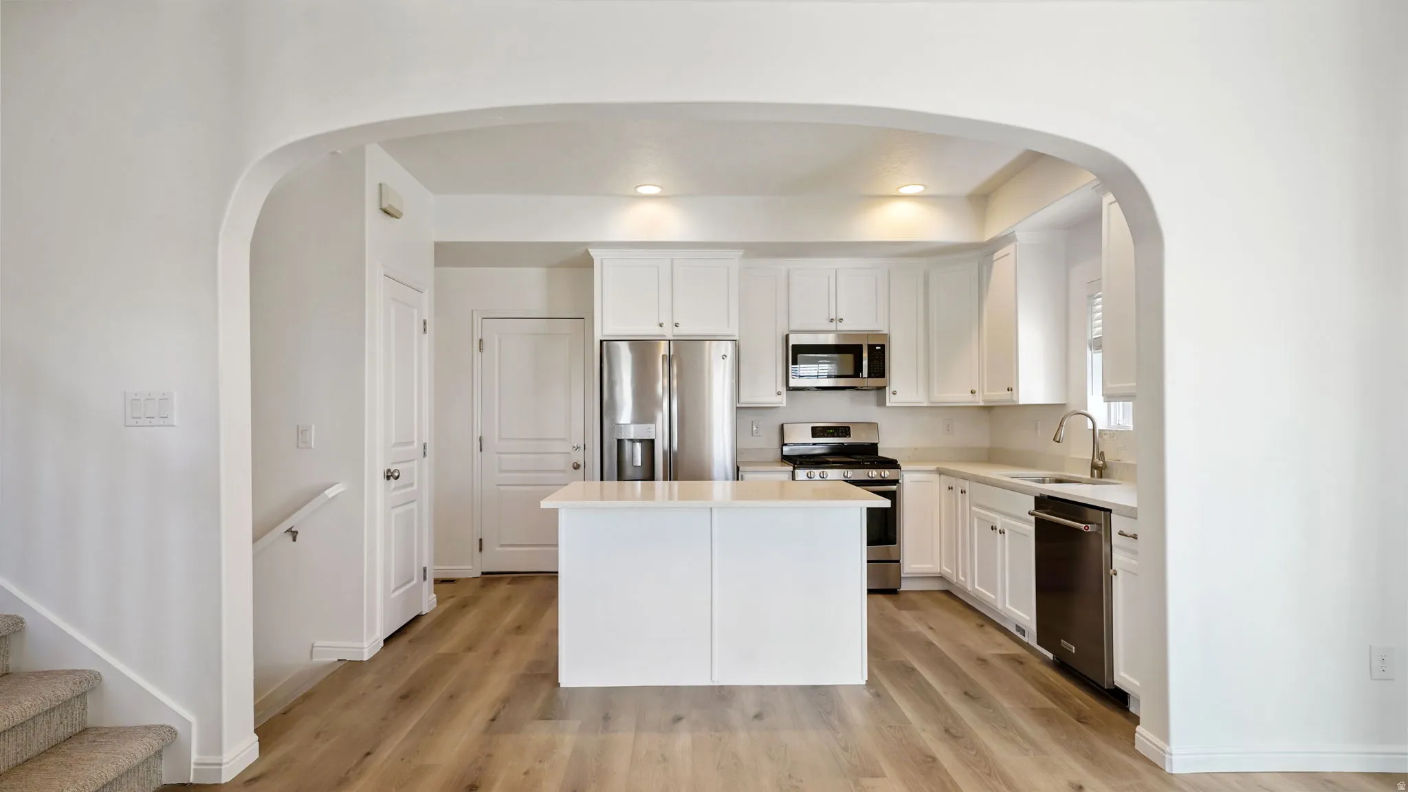 Kitchen featuring an arched entryway, wood-finish flooring, white cabinetry, stainless steel appliances, and a central island