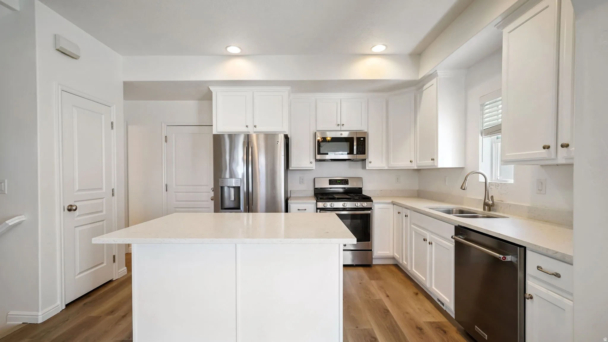 Kitchen featuring a central island with a light-toned countertop, white cabinetry, stainless steel appliances, wood-finish flooring, and recessed lighting