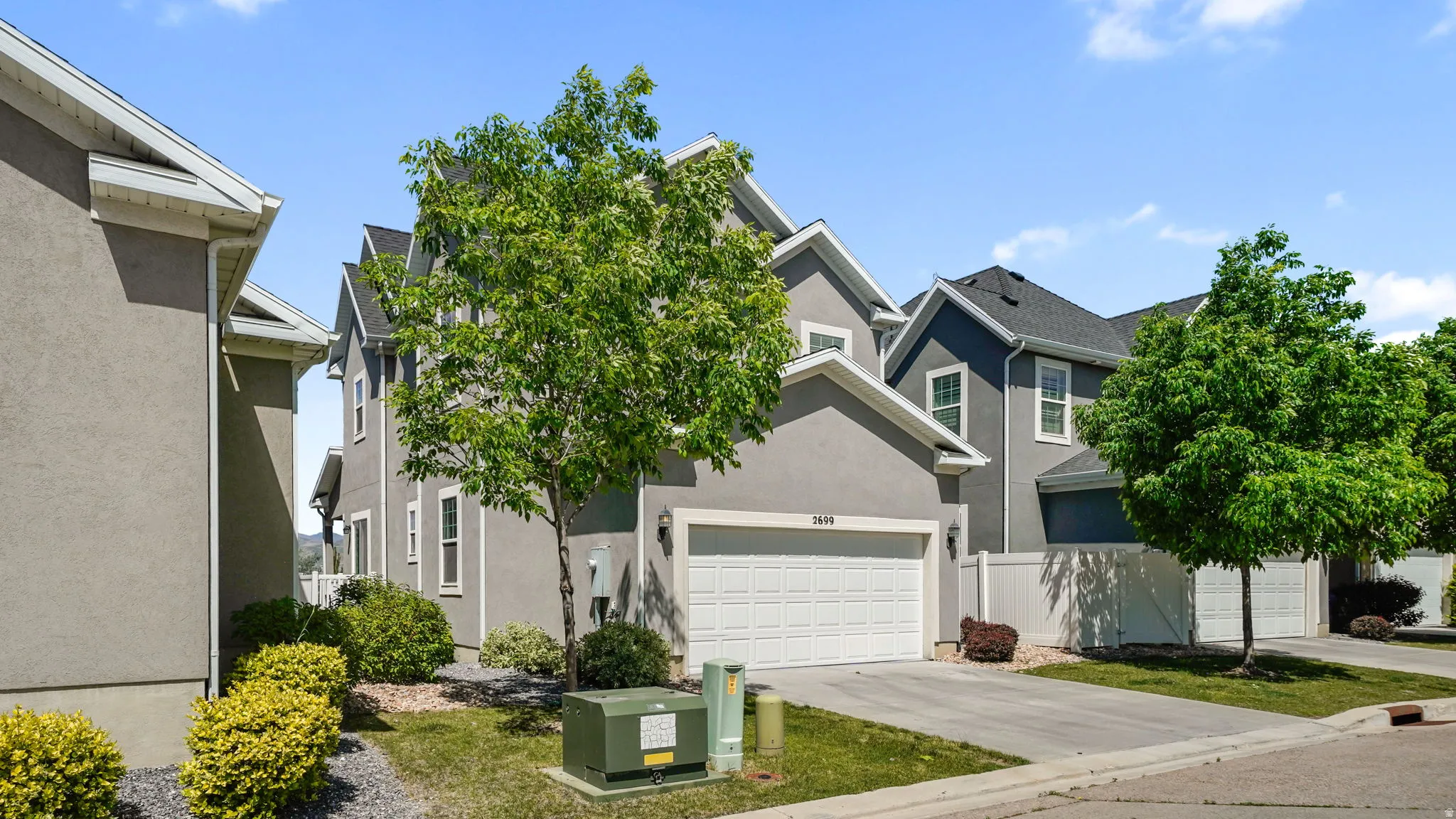 Contemporary townhouse featuring a light gray stucco exterior, white garage door, and a mature deciduous tree