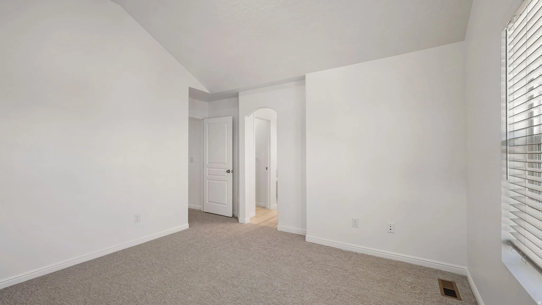 Carpeted room featuring a vaulted ceiling and window with horizontal blinds