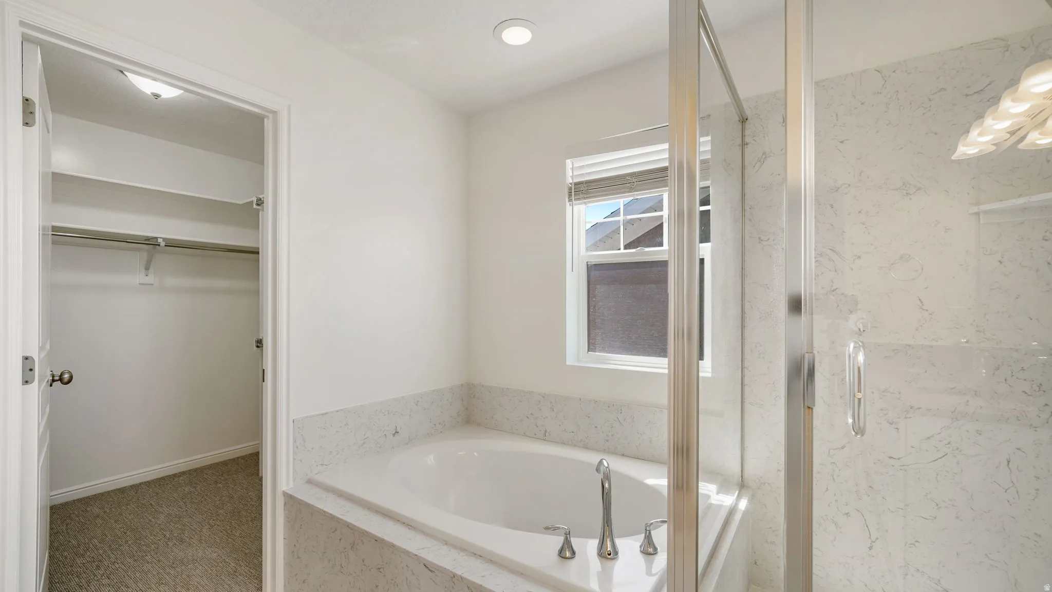 Bathroom featuring a built-in soaking tub with a stone-finish surround, separate glass-enclosed shower, and a privacy window with blinds