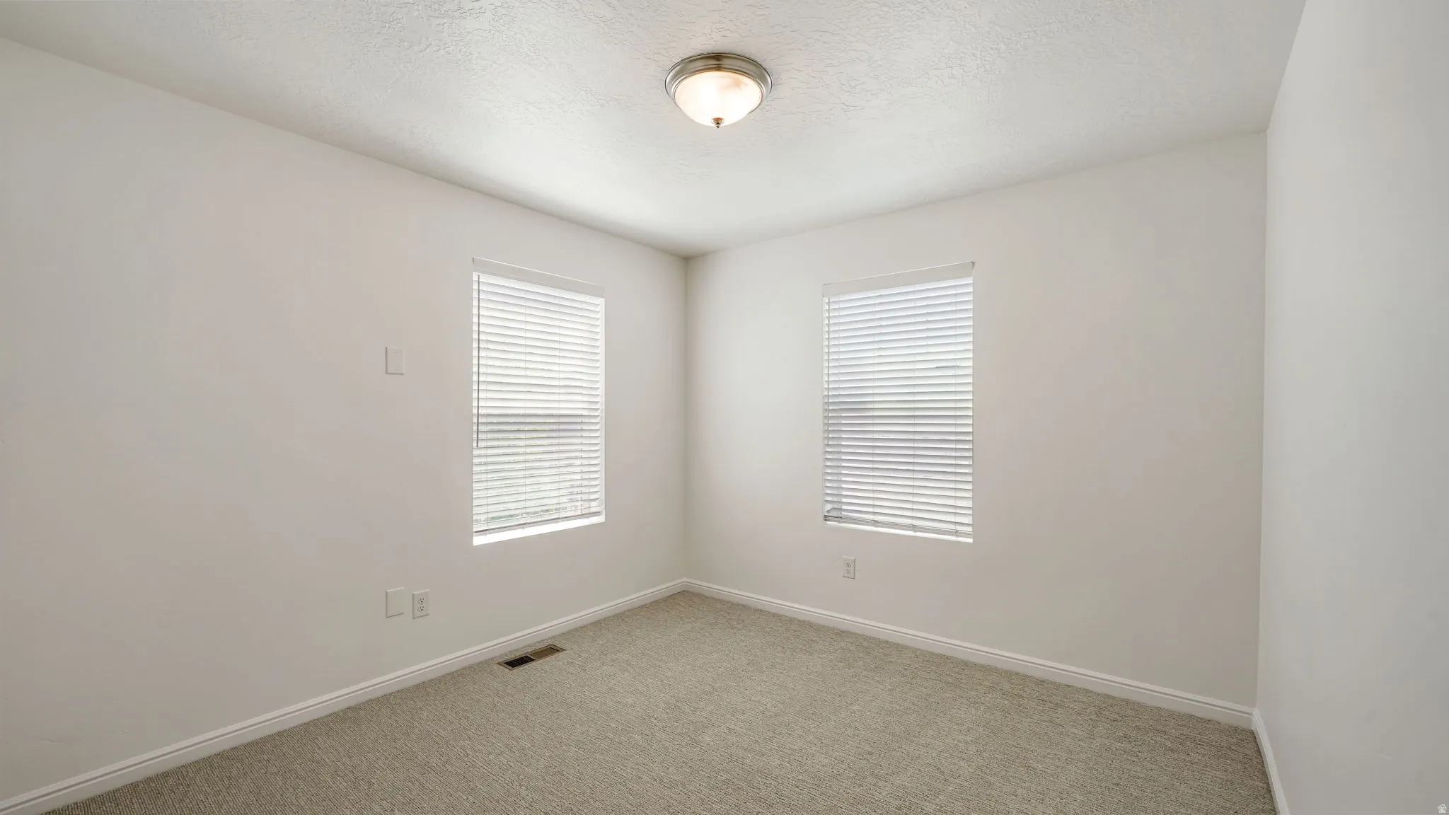 Neutral-toned carpeted room featuring two windows with blinds