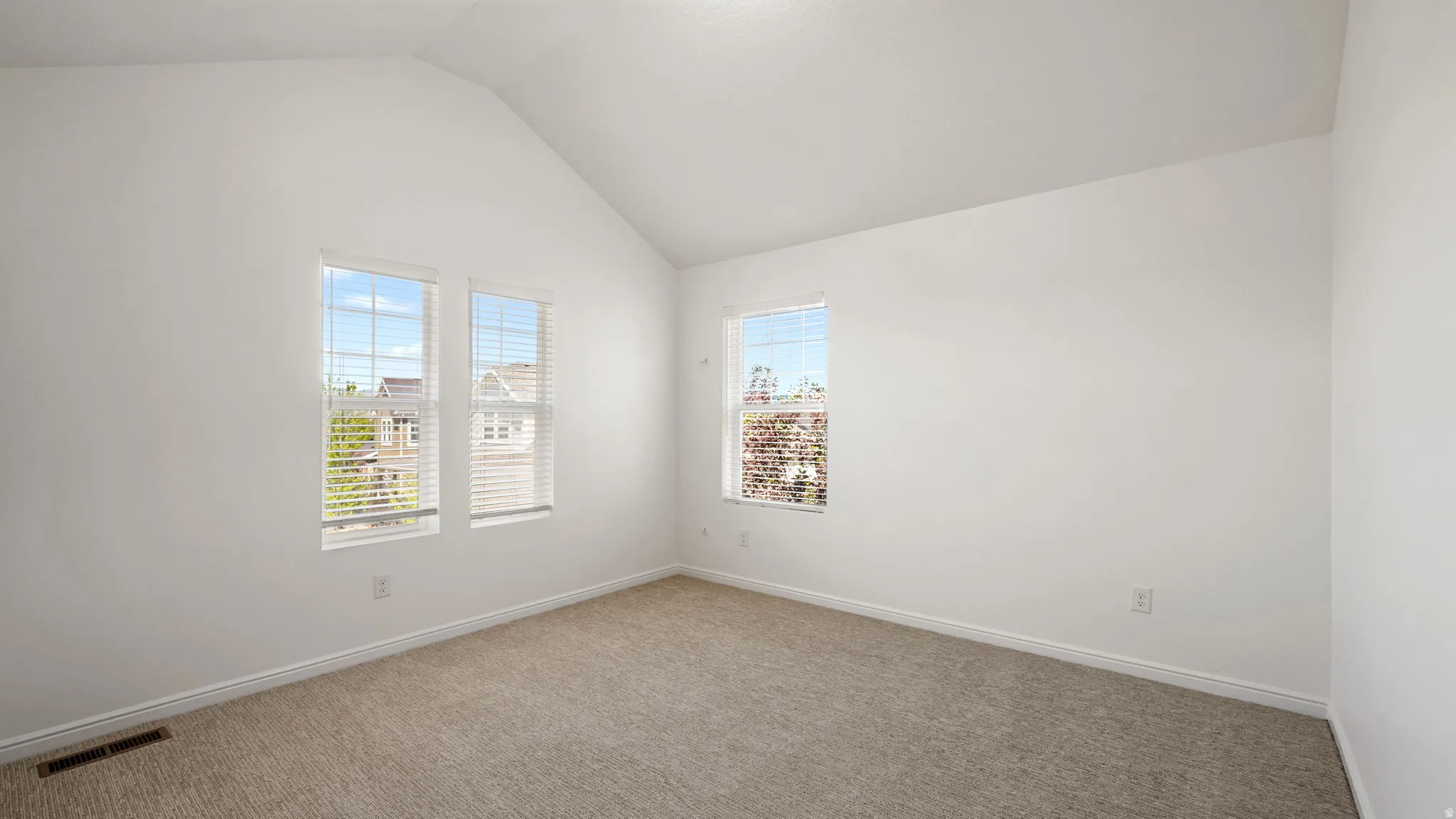 Spacious room featuring vaulted ceilings, light-toned carpeting, and multiple windows providing ambient light