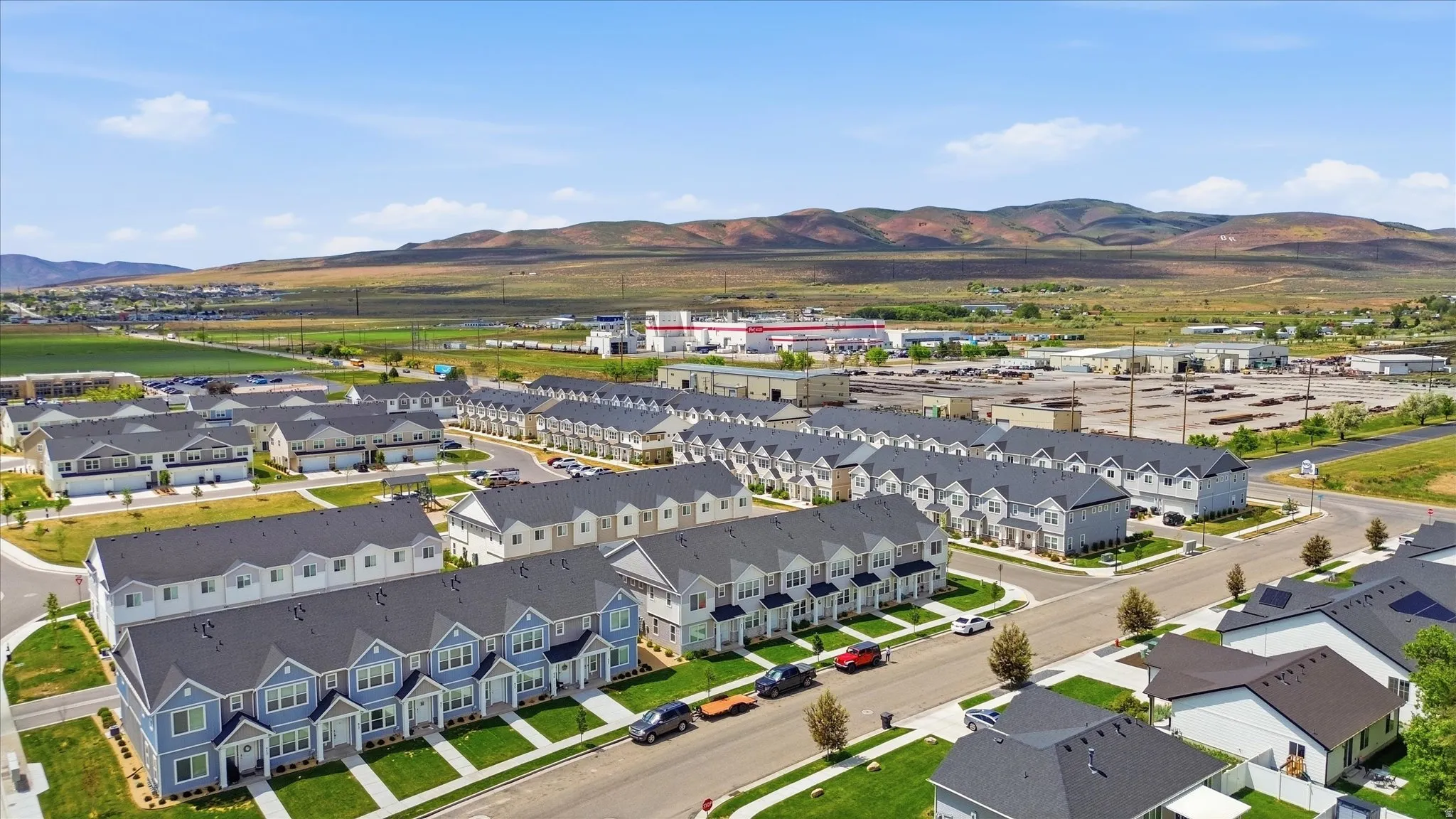 An aerial perspective showcasing a residential development featuring uniform townhome architecture, landscaped grounds, and a backdrop of distant hills
