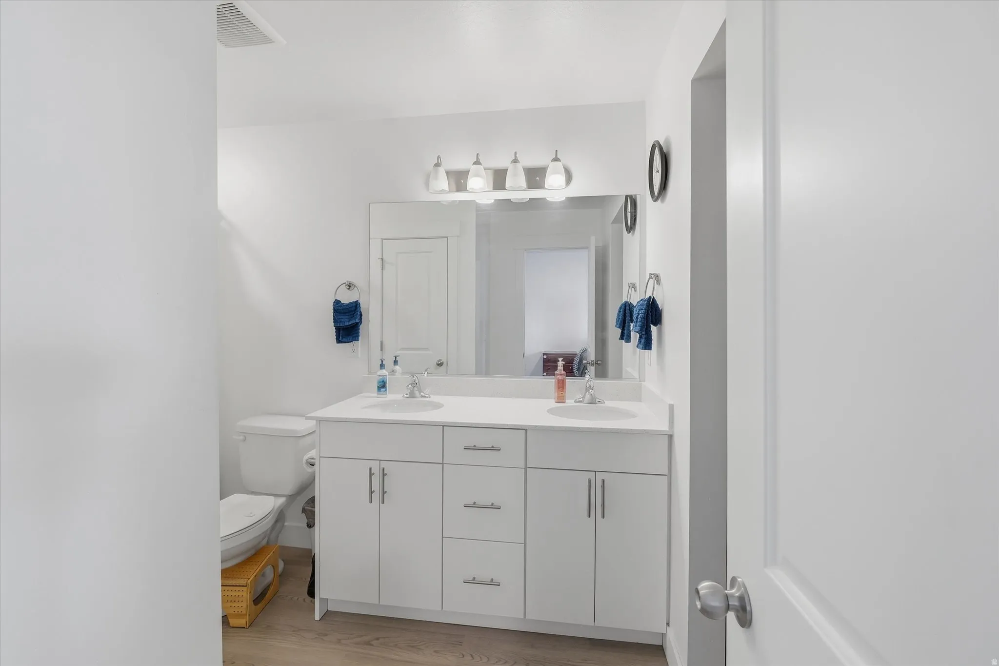 Bright bathroom featuring a dual vanity with white cabinetry, integrated sinks, and brushed nickel hardware