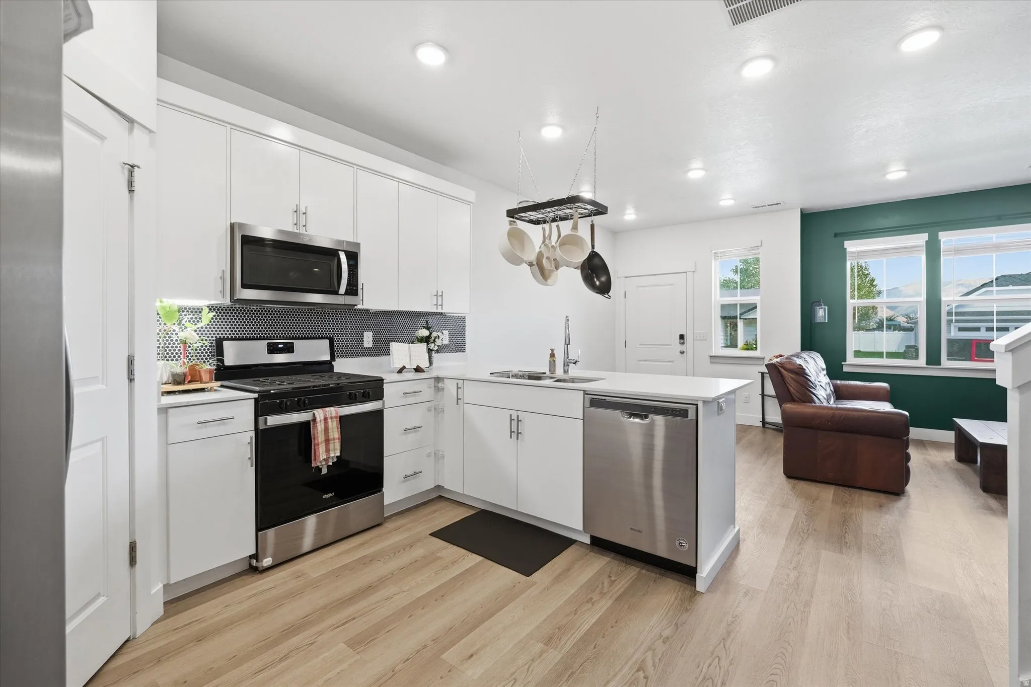 Modern kitchen featuring white cabinetry, light countertops, stainless steel appliances, and a black patterned backsplash