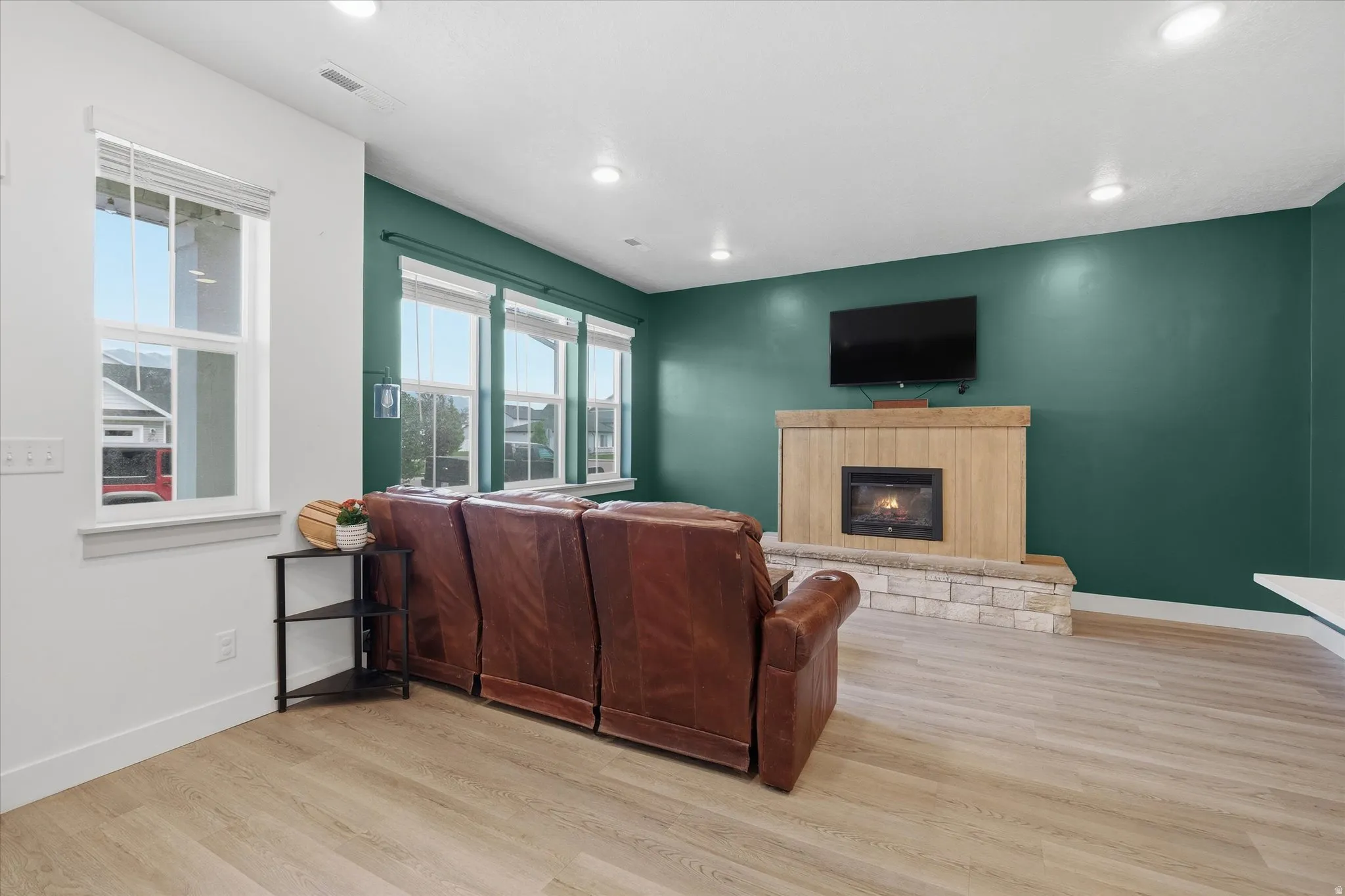 Living area featuring a gas fireplace with a stone surround and wood mantel, light wood-finish flooring, recessed lighting, and multiple windows