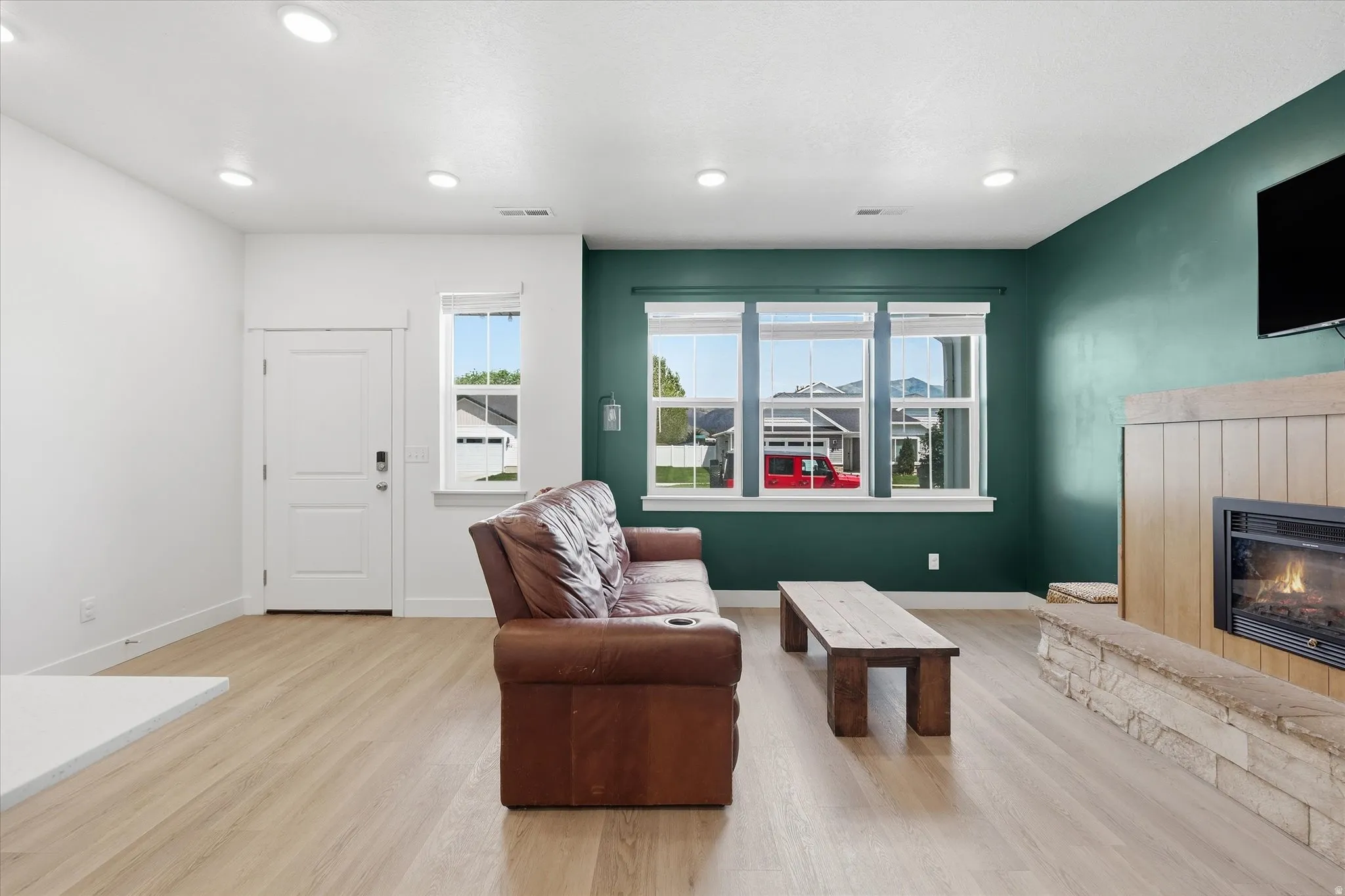 Living area featuring wood-finish flooring, recessed lighting, and a prominent fireplace with a stone hearth and wood surround
