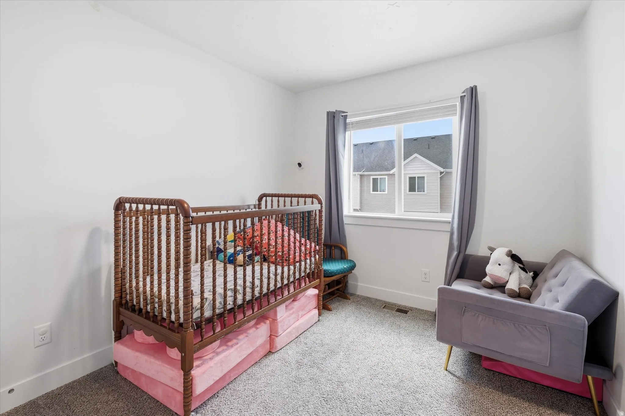 Bright room featuring white walls, gray carpet flooring, a large window with white trim, and gray curtains