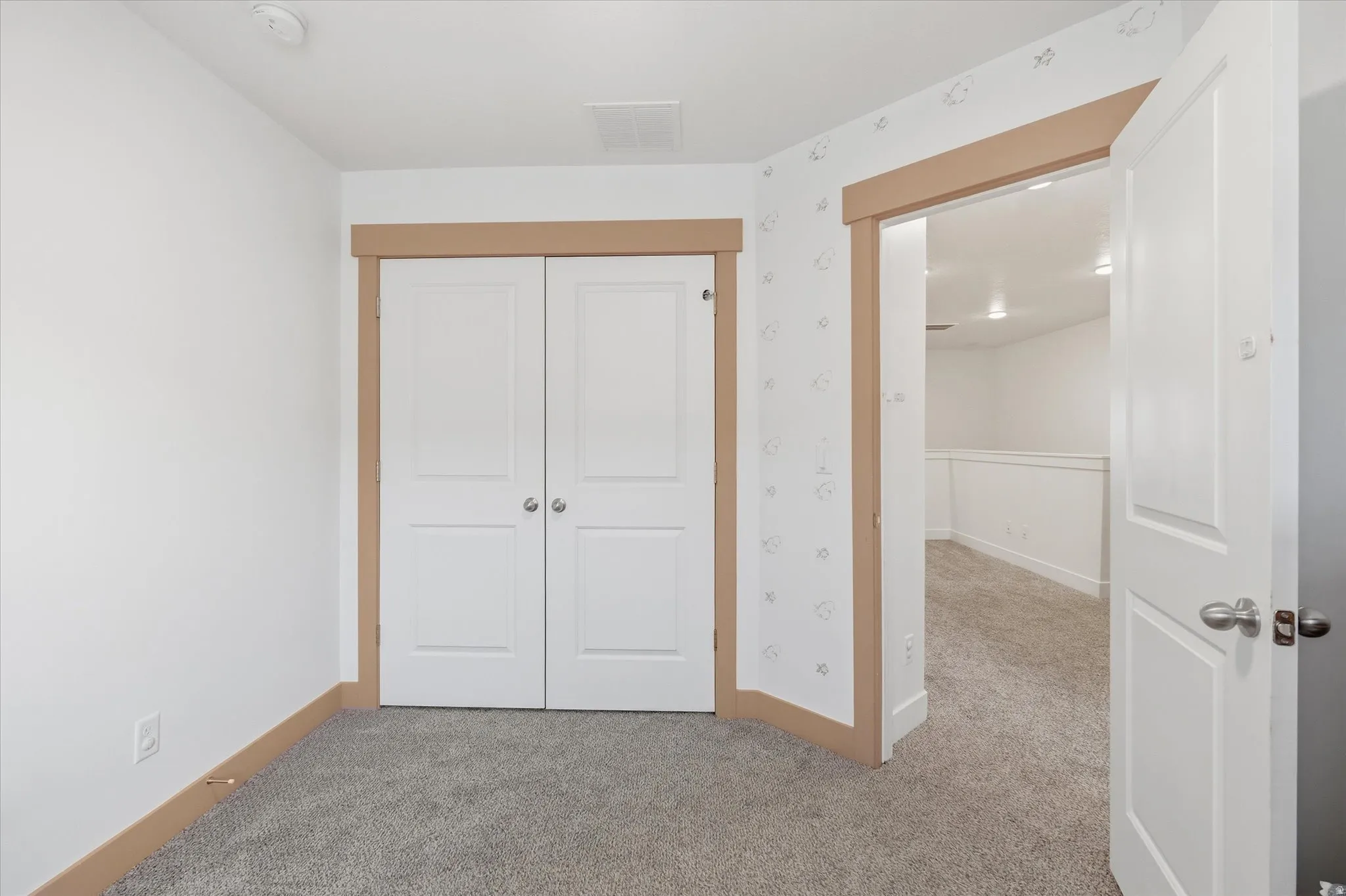 Carpeted room featuring white walls, a built-in double-door closet with panel detailing, and natural wood-finish trim