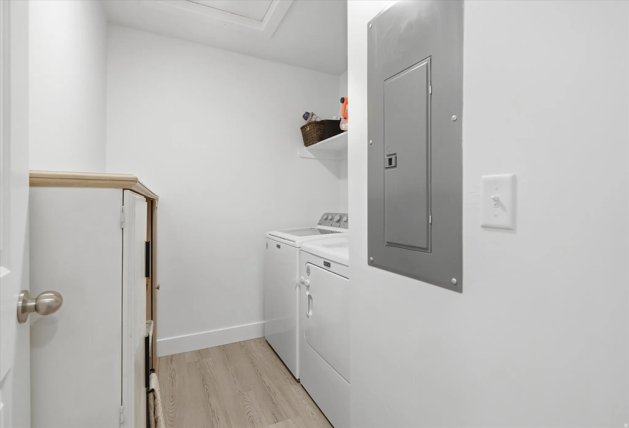 Dedicated laundry area featuring wood-finish flooring, white walls, and a built-in white cabinet with a light-toned wood-finish top