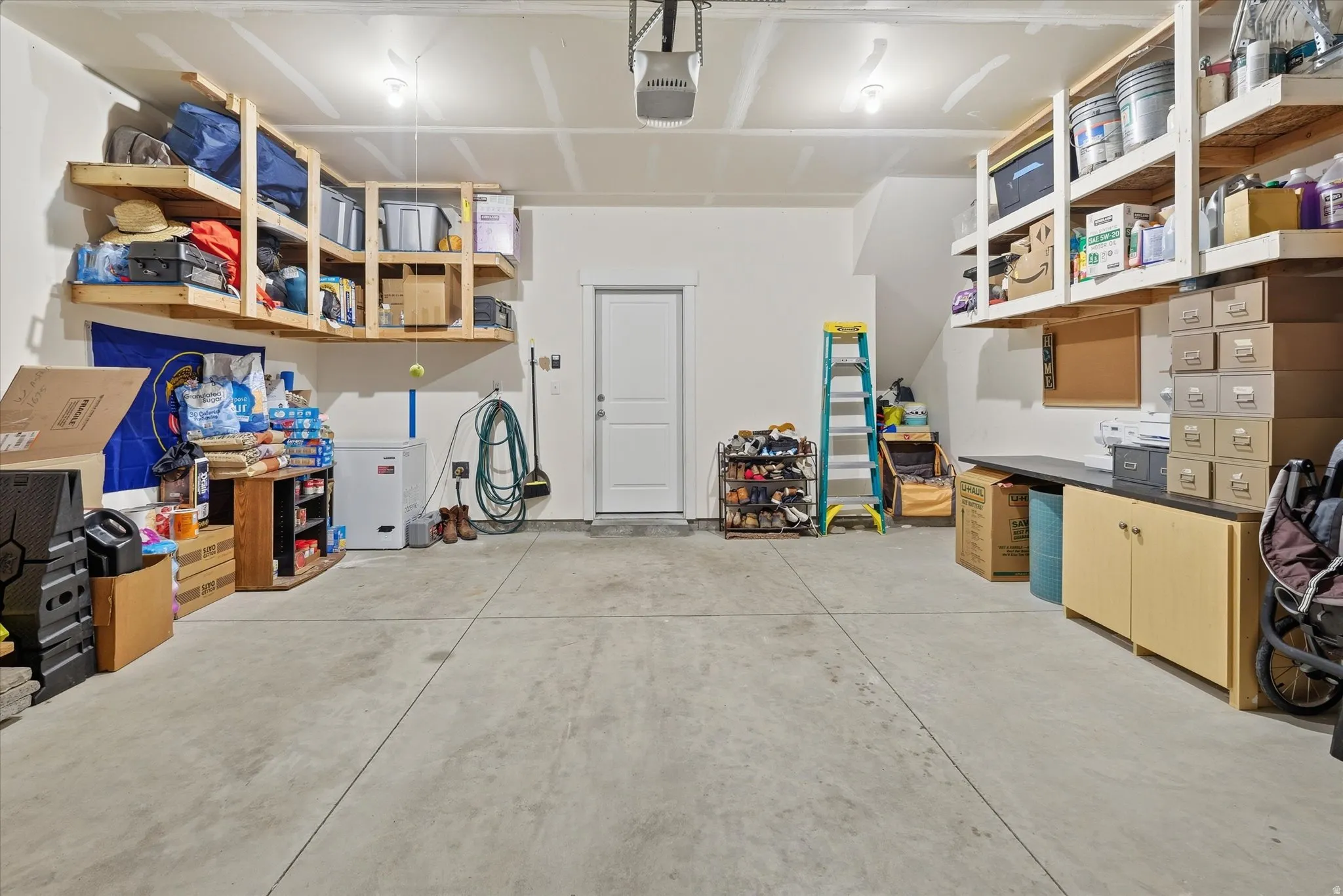 Spacious garage featuring a concrete floor, built-in overhead shelving, a work surface with cabinetry, a pedestrian door, and overhead lighting