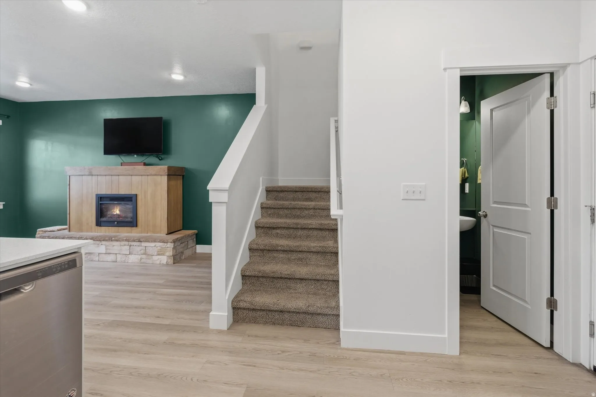 Carpeted staircase with white balustrade, wood-finish flooring, and a fireplace featuring a stone base and wood-finish surround
