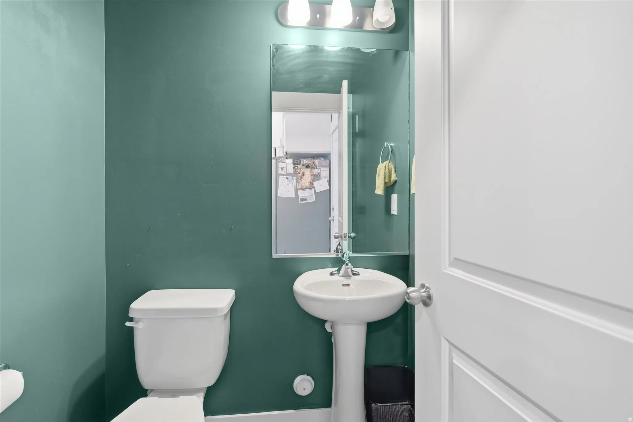 Pedestal sink with chrome fixtures, framed mirror, and three-light vanity bar