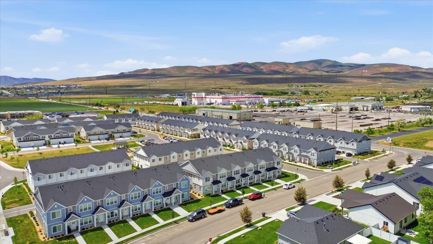 An aerial perspective showcasing a residential development featuring uniform townhome architecture, landscaped grounds, and a backdrop of distant hills