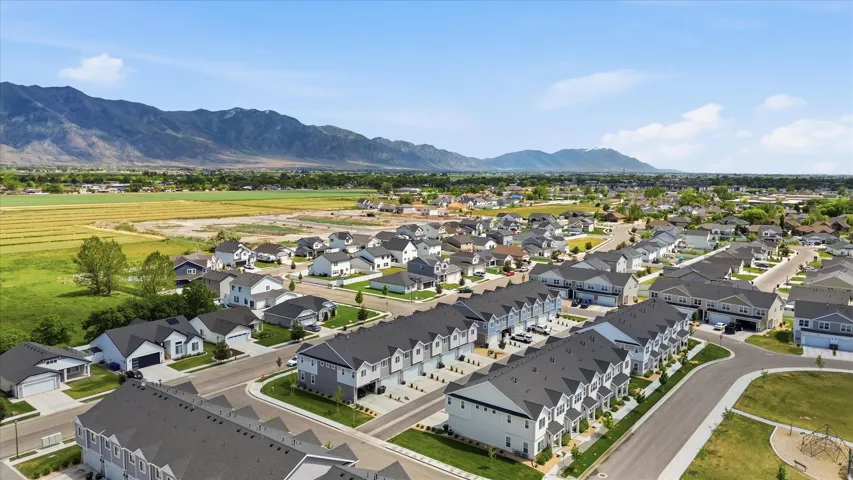 New construction residential development featuring a mix of detached single-family homes and townhomes, surrounded by agricultural fields and distant mountains