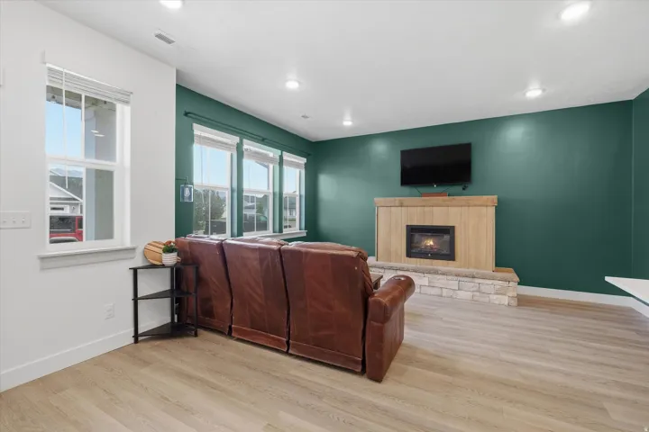 Living area featuring a gas fireplace with a stone surround and wood mantel, light wood-finish flooring, recessed lighting, and multiple windows