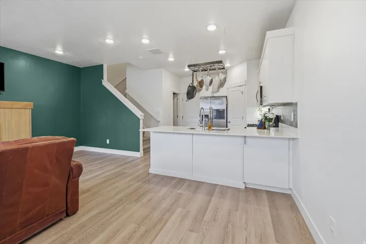 Open-concept kitchen featuring white cabinetry, a large center island with a sink, stainless steel appliances, and a mosaic tile backsplash