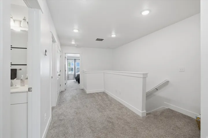 Carpeted hallway with white walls and trim, featuring recessed ceiling lighting, a partial staircase with a handrail, and white paneled doors