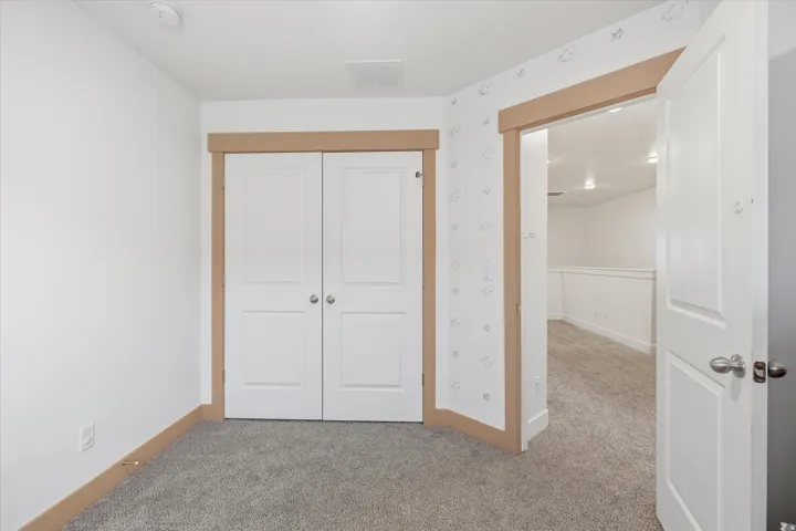 Carpeted room featuring white walls, a built-in double-door closet with panel detailing, and natural wood-finish trim
