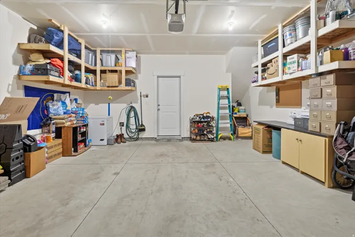 Spacious garage featuring a concrete floor, built-in overhead shelving, a work surface with cabinetry, a pedestrian door, and overhead lighting